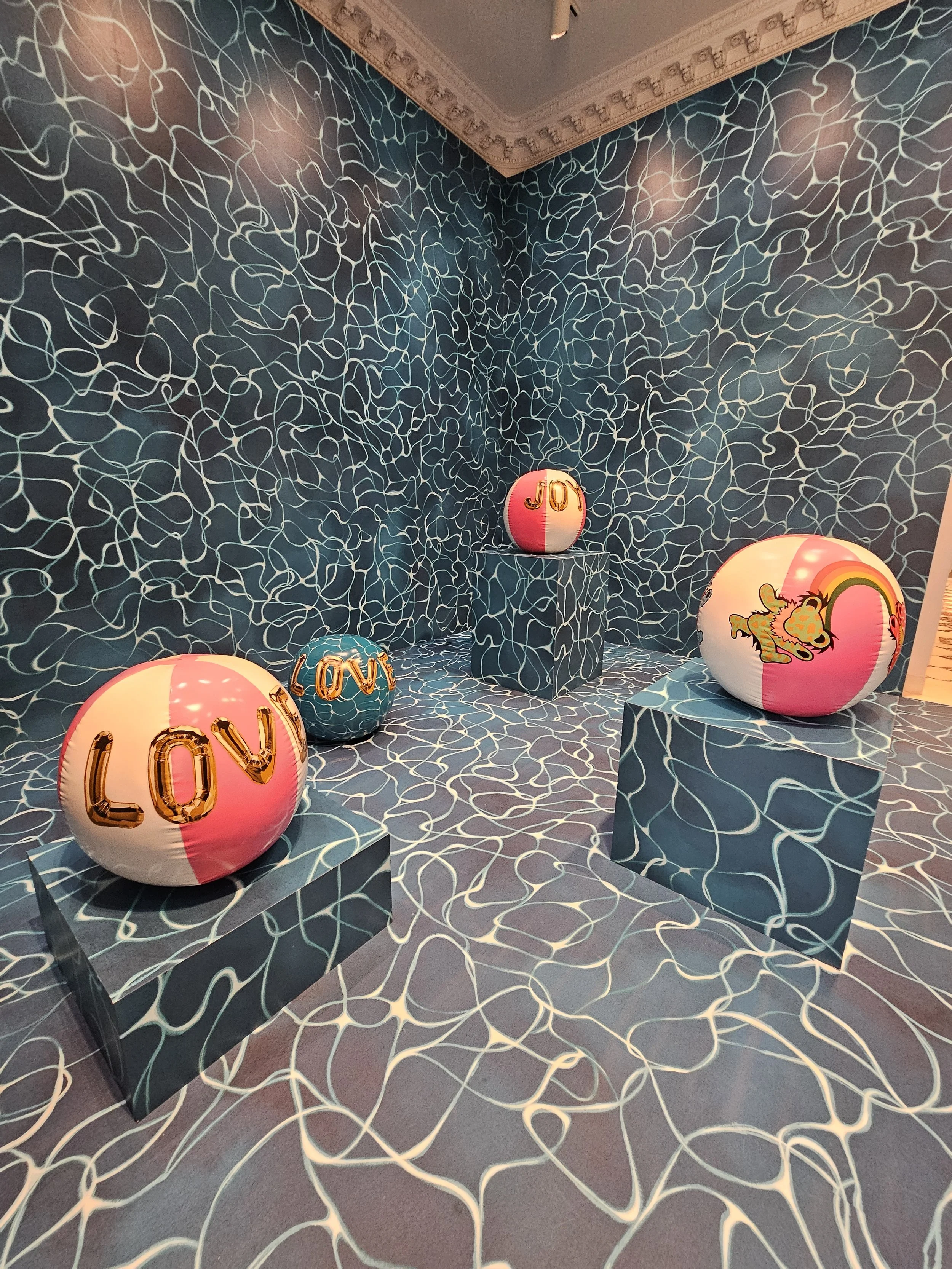 Art installation featuring colorful spheres with words and images, set against a patterned blue and white background and floor.