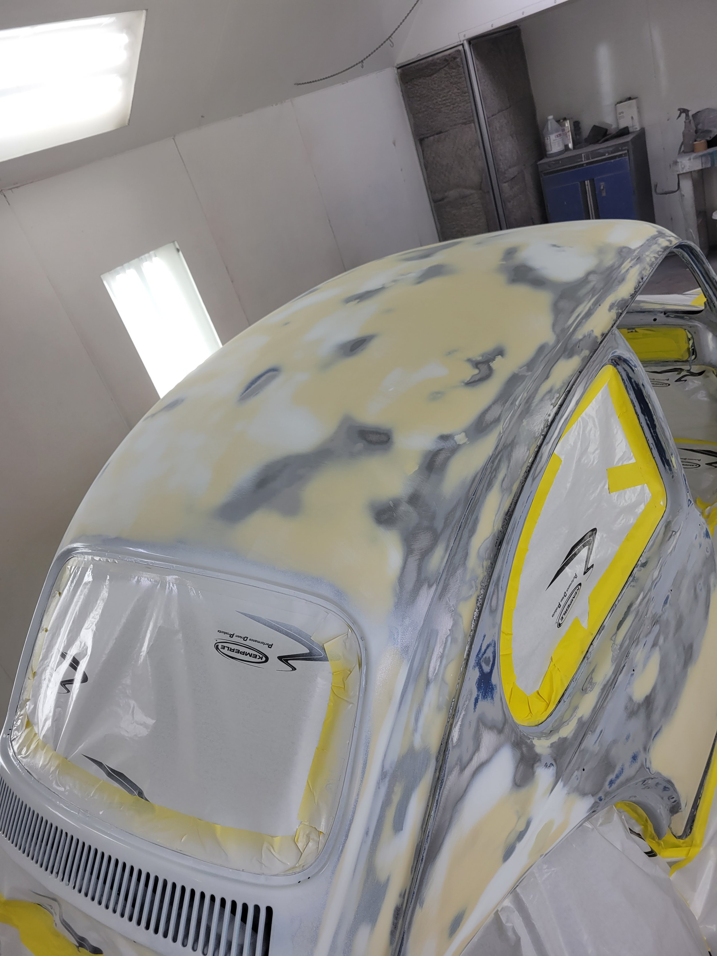 A vintage car undergoing bodywork repair with primer and sanding, in a workshop