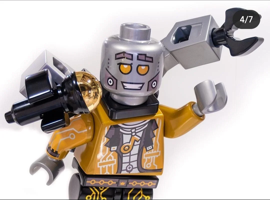 LEGO minifigure with a robot head, wearing a yellow jacket, holding a black and gold futuristic weapon, and making a playful wave.