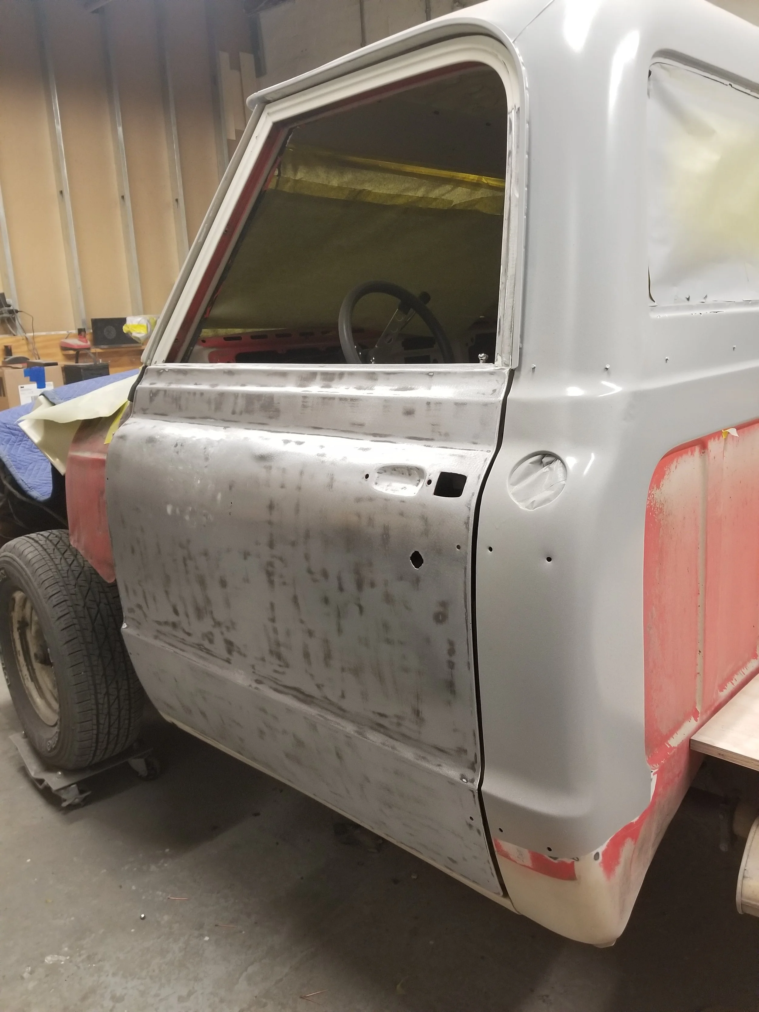 A classic van undergoing restoration, with a partially sanded and primed body, parked inside a workshop.
