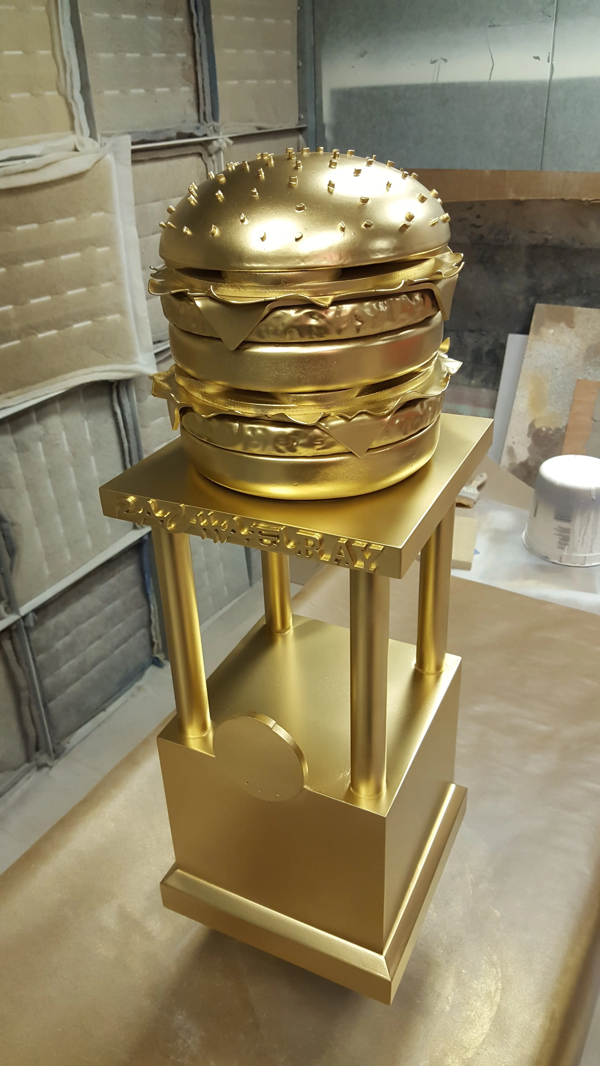 A gold-colored, burger-shaped sculpture on a stand.