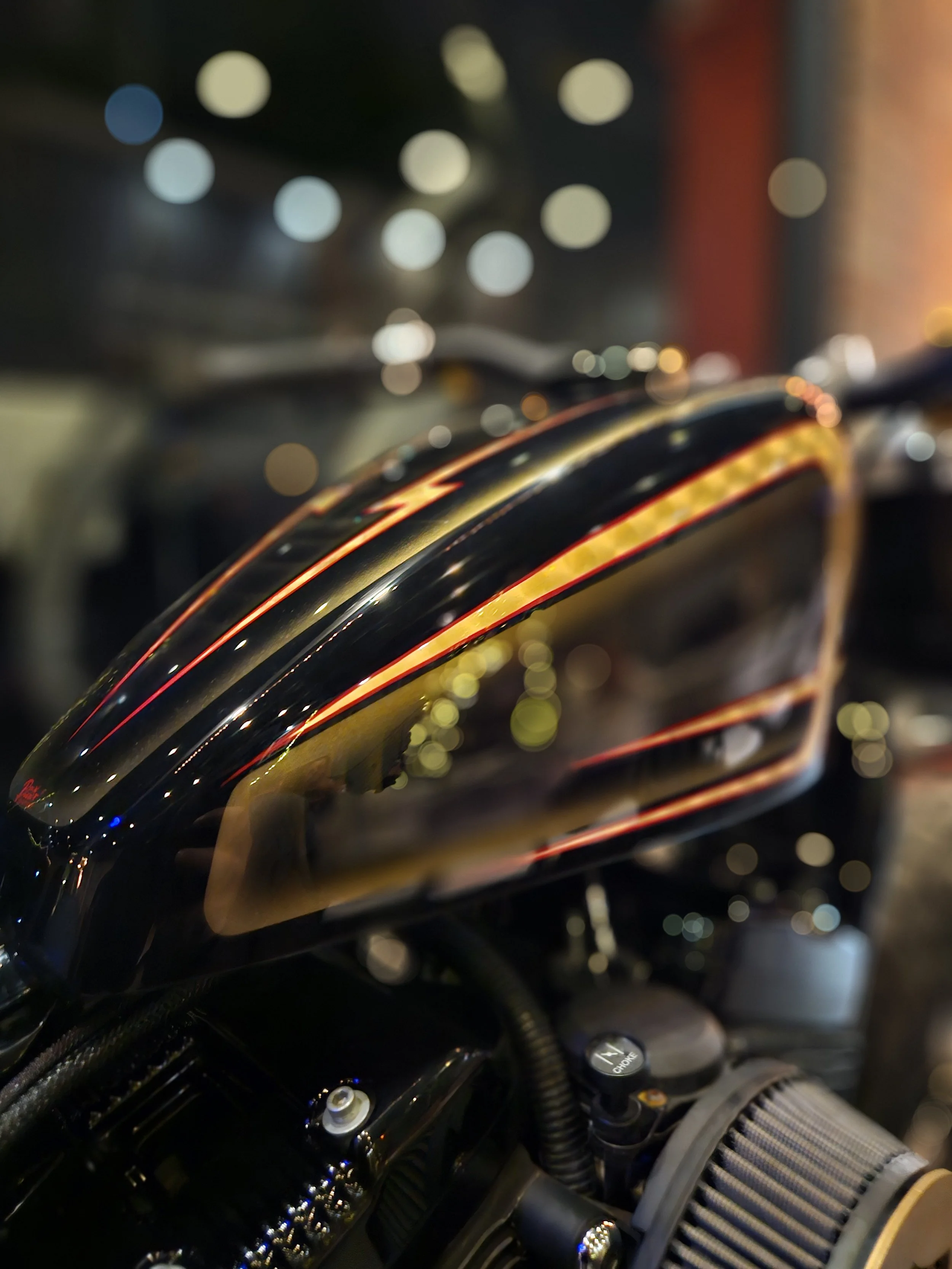 Close-up of a black motorcycle with orange and yellow accents, with blurred colorful lights in the background.