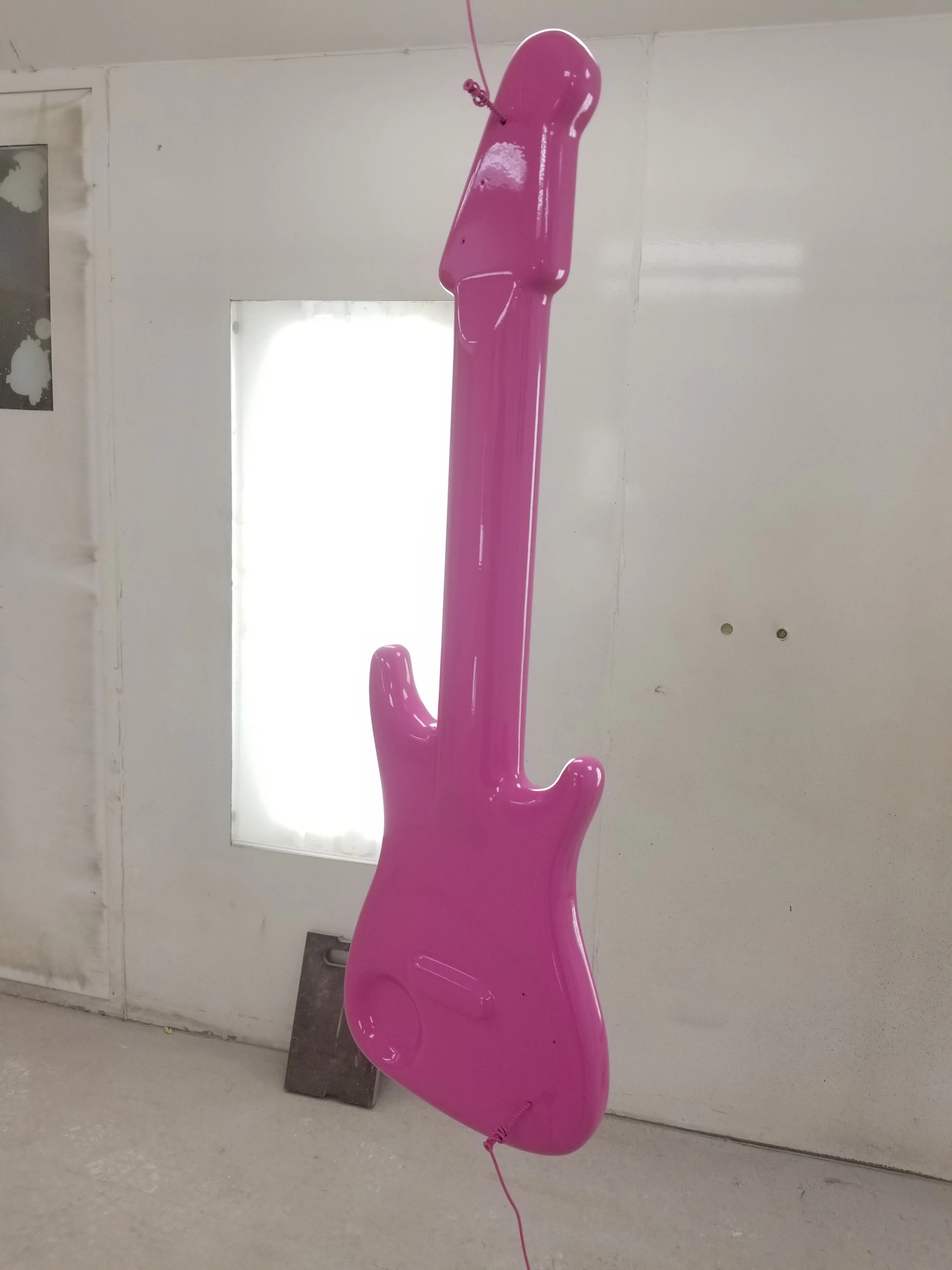 Pink inflatable guitar leaning against a white wall in a room.