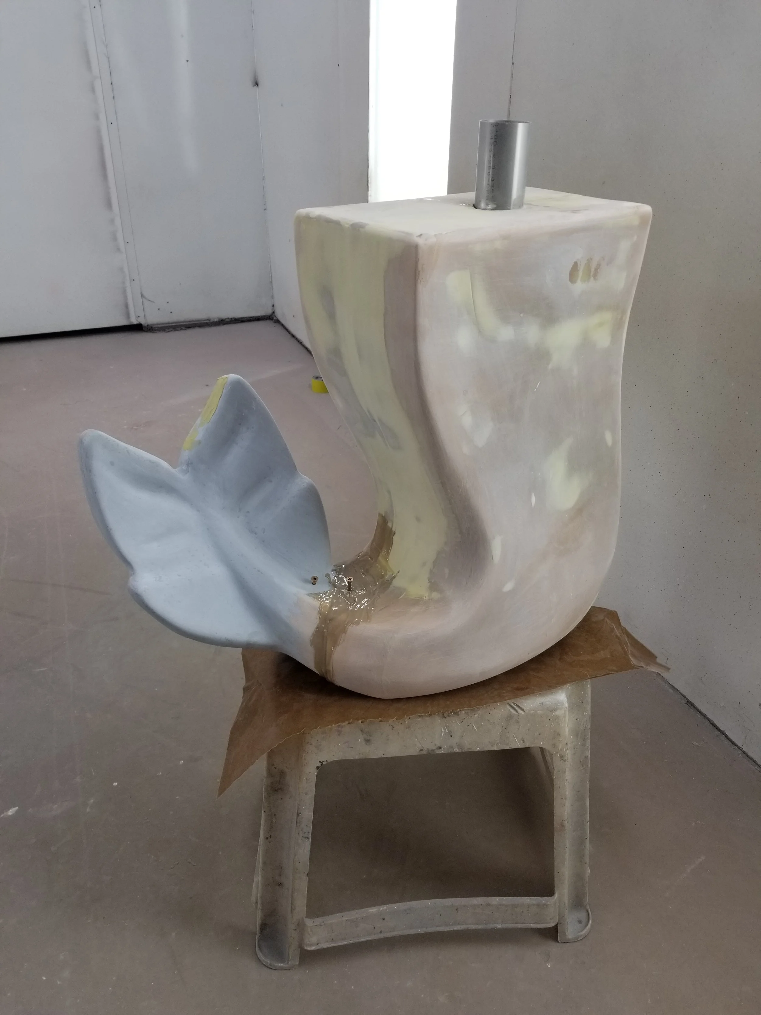 A partially finished LEGO mermaid sculpture, placed on a small stool in a workshop setting.