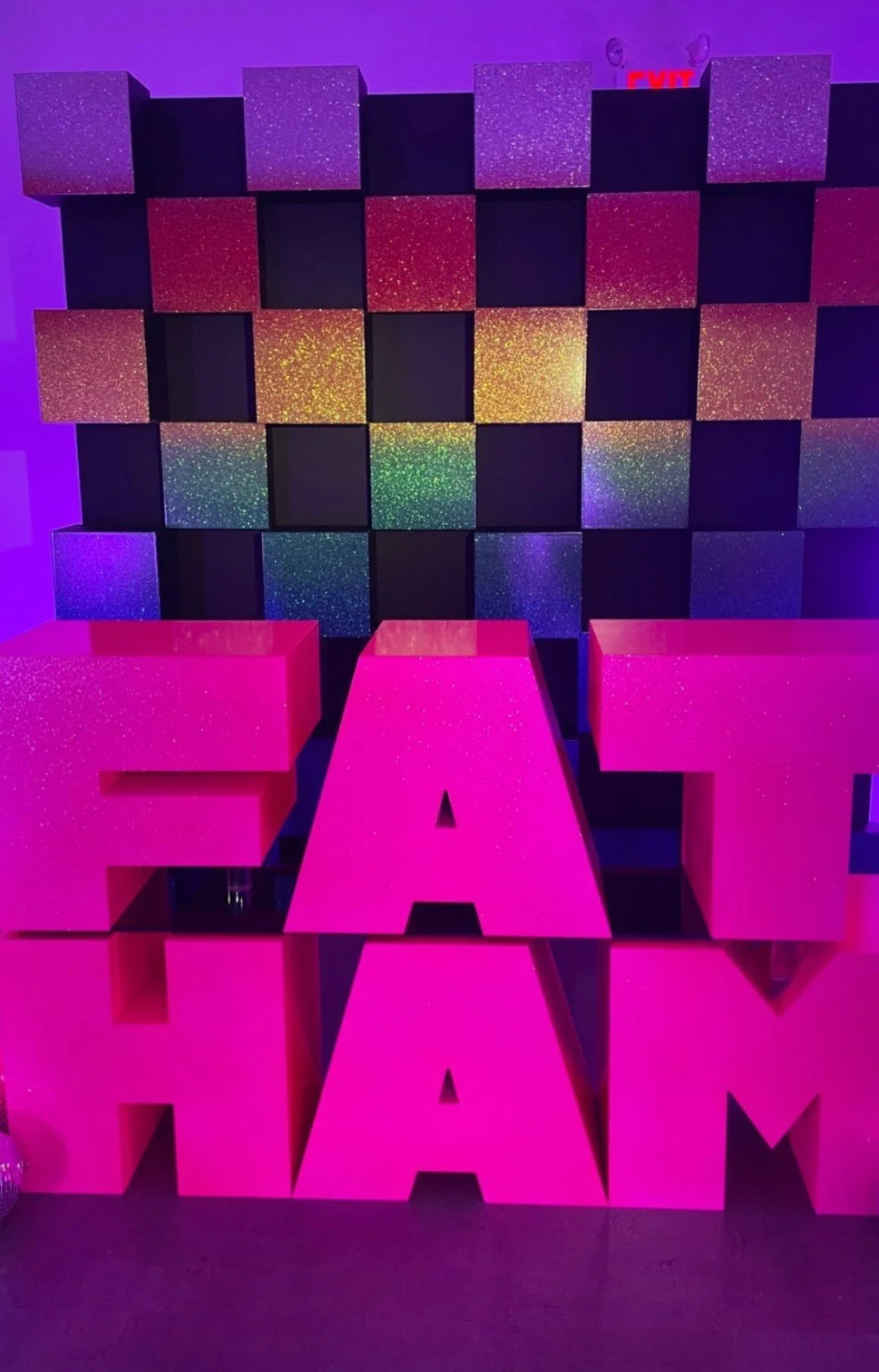 Decorative wall with black and glittery pink cubes and large pink blocks spelling out "EAT CAKE" in front.