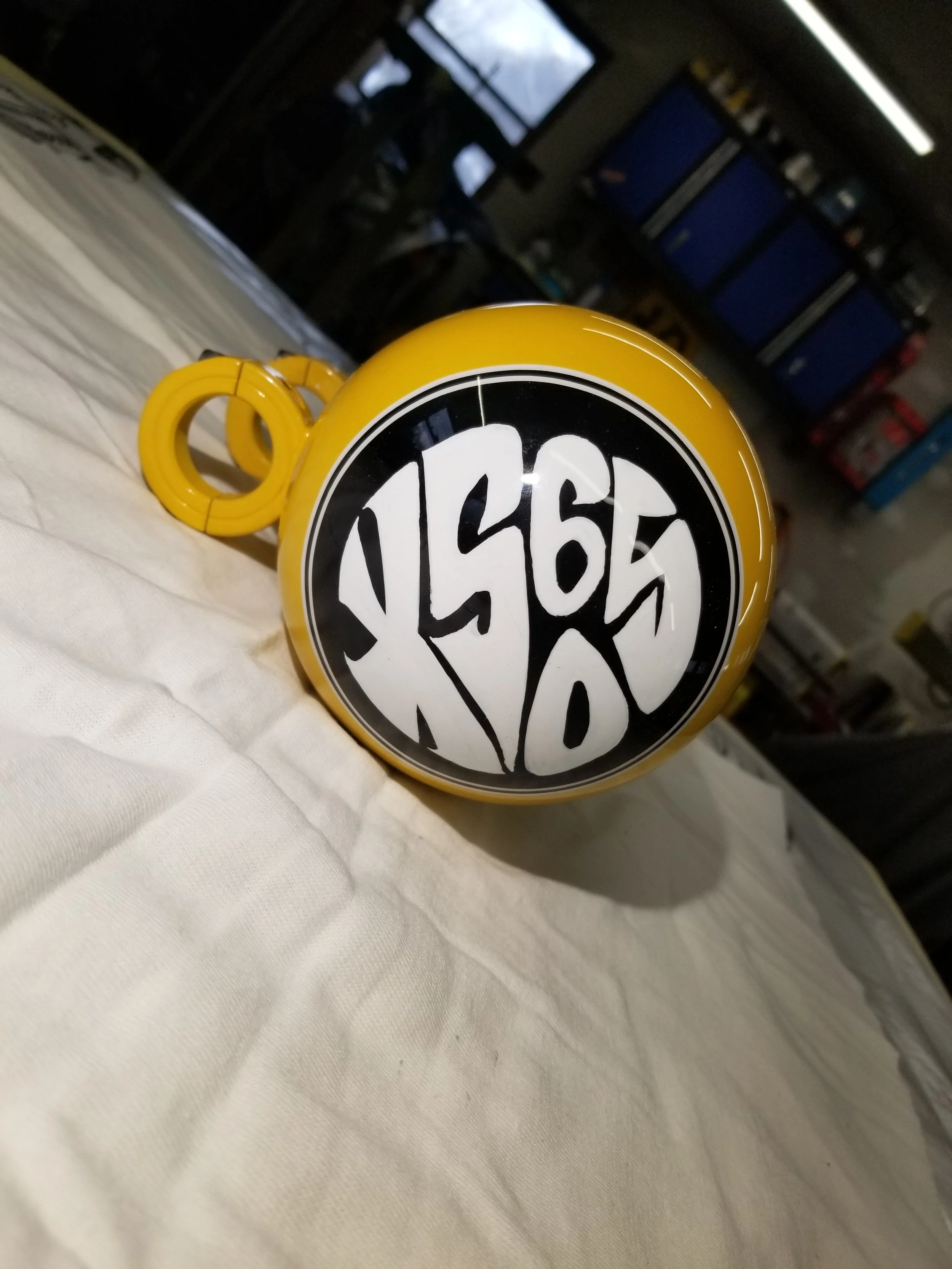 Yellow mug with a black and white graffiti-style design that reads 'XS 650' in a circular pattern, placed on a white fabric surface.