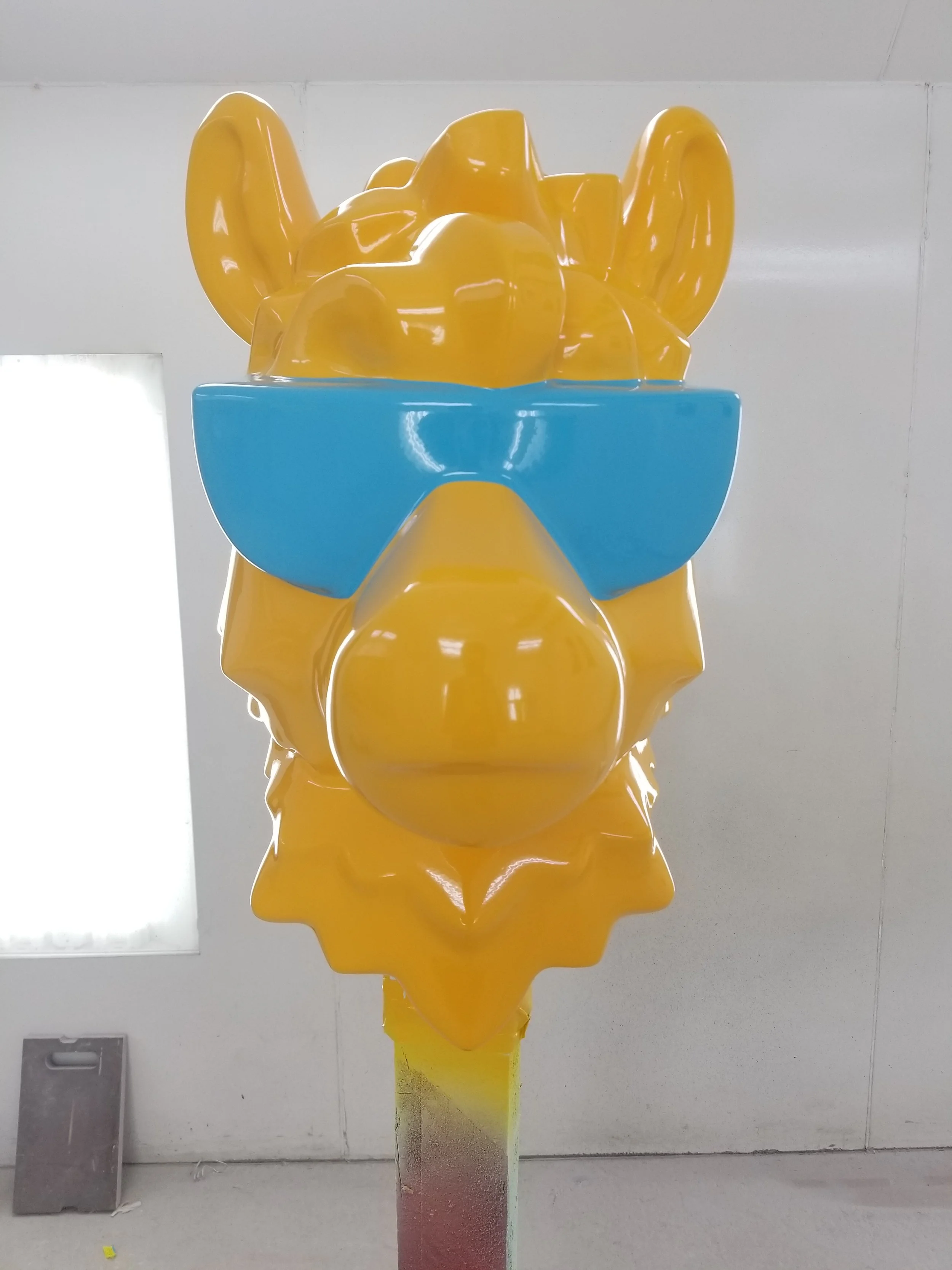 A large, stylized yellow LEGO camel statue with blue sunglasses