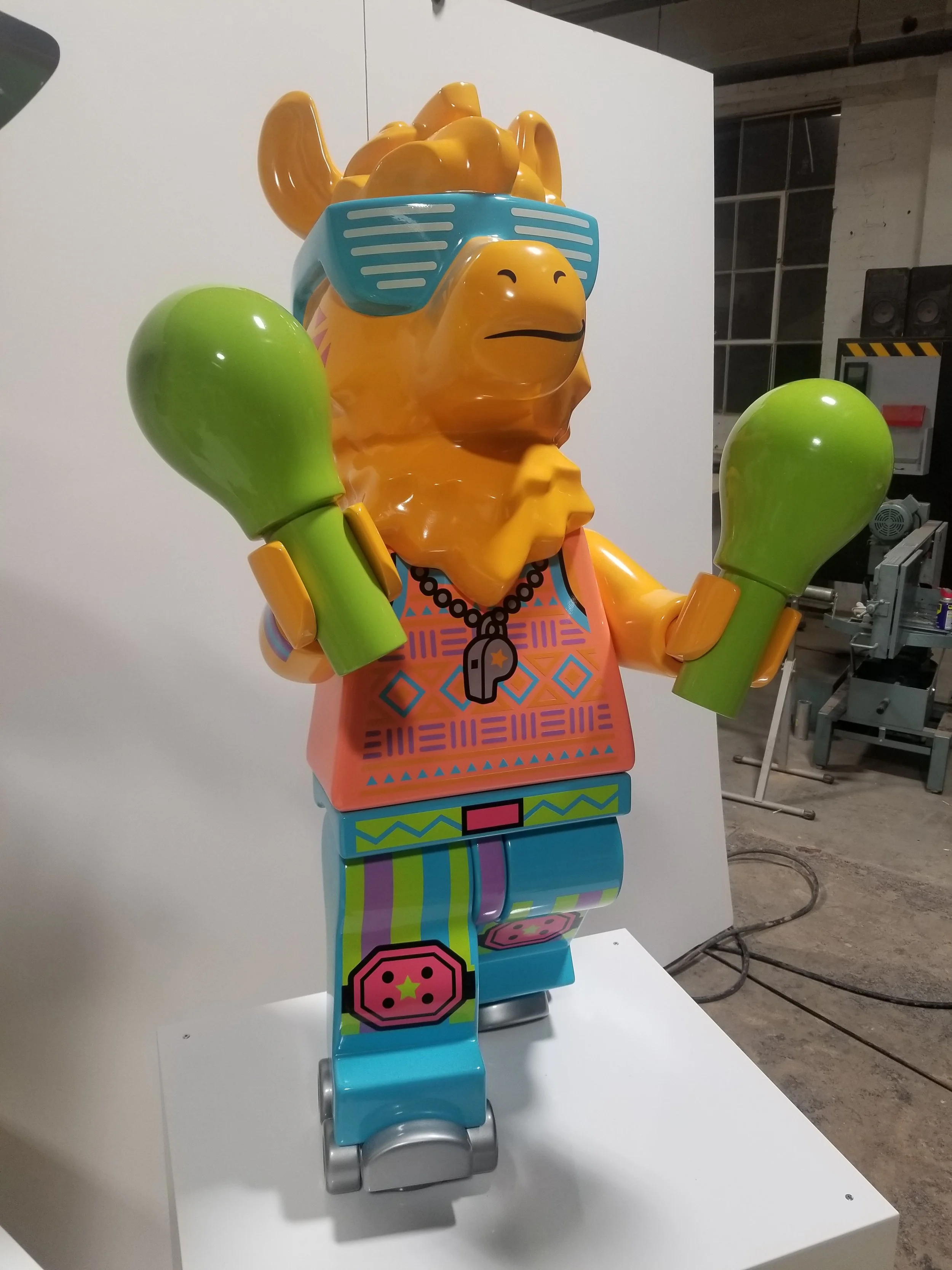 Colorful robot sculpture of a camel wearing sunglasses and maracas, standing on a white platform.