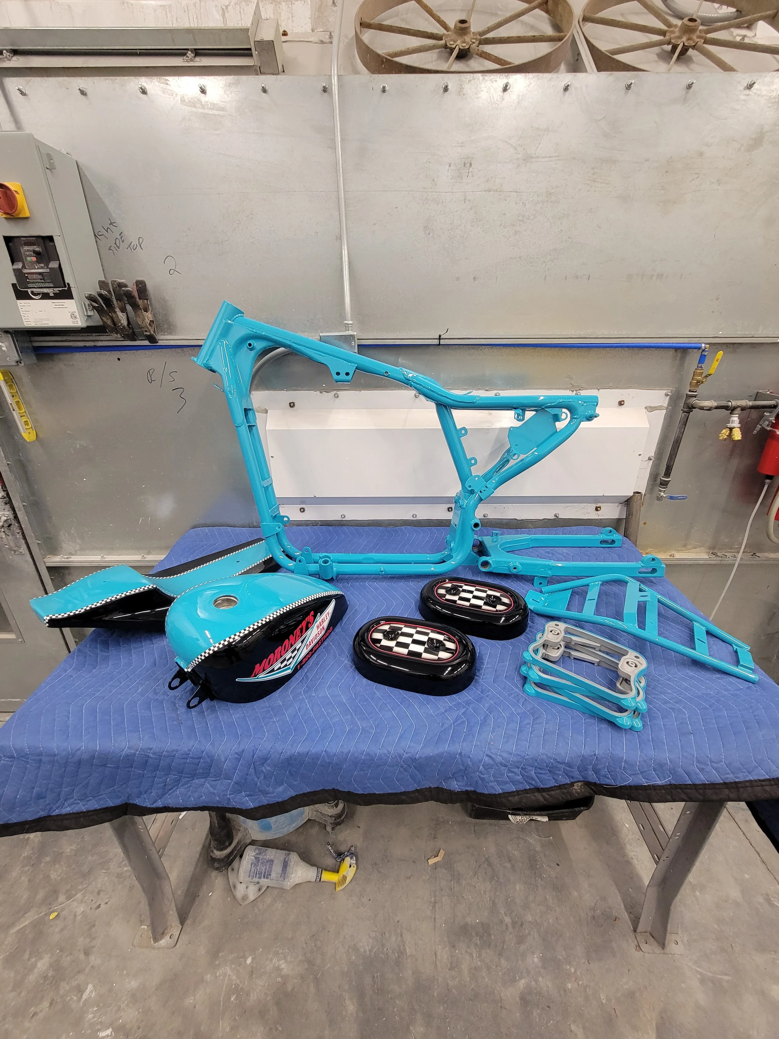Disassembled blue motorcycle frame and accessories on a table in a workshop.