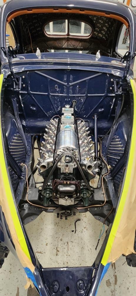View of a classic race car with the engine and chassis exposed, painted in blue with yellow and orange accents, inside a workshop.