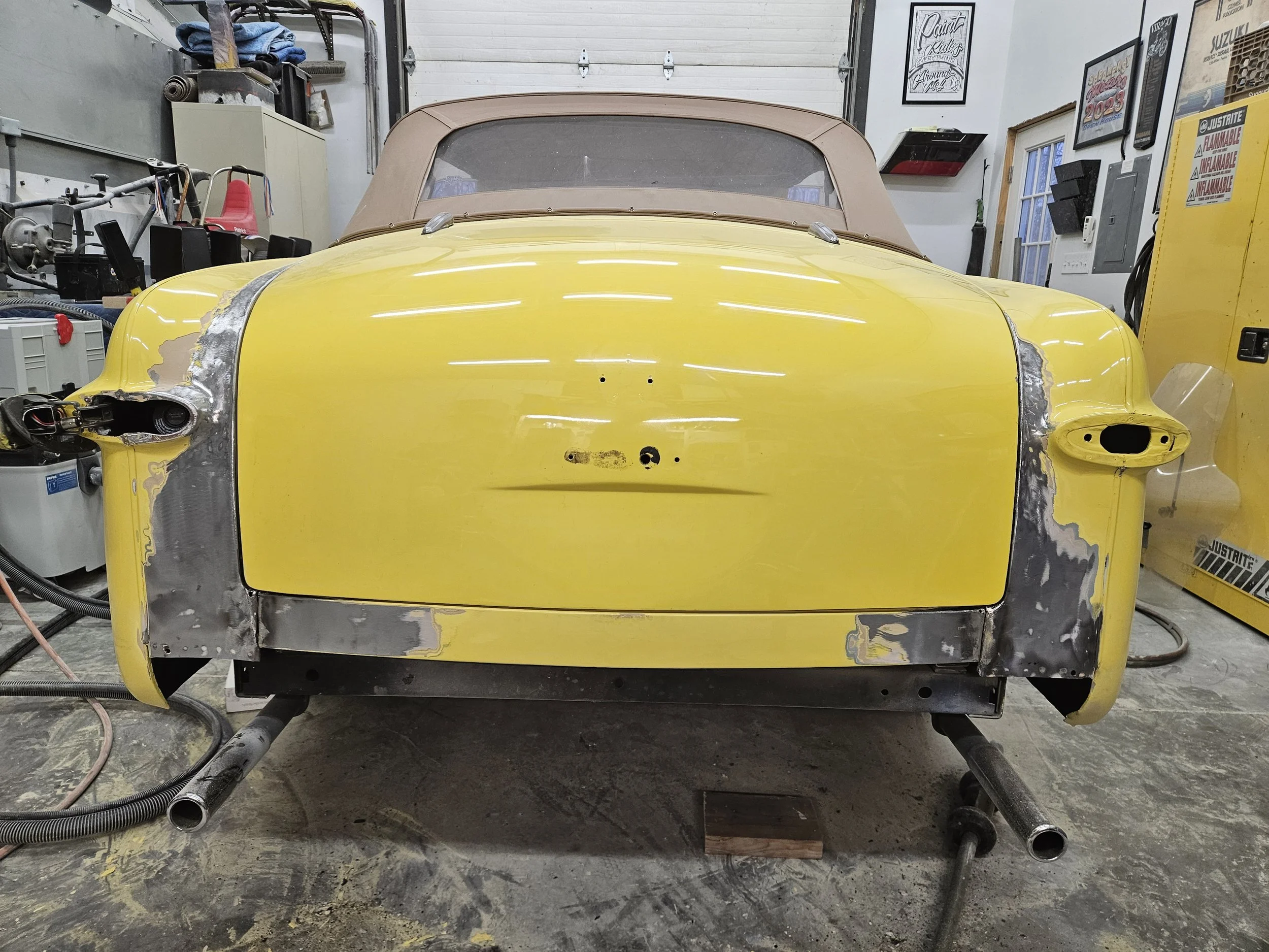 Yellow vintage car with missing and unfinished parts in a garage or workshop.