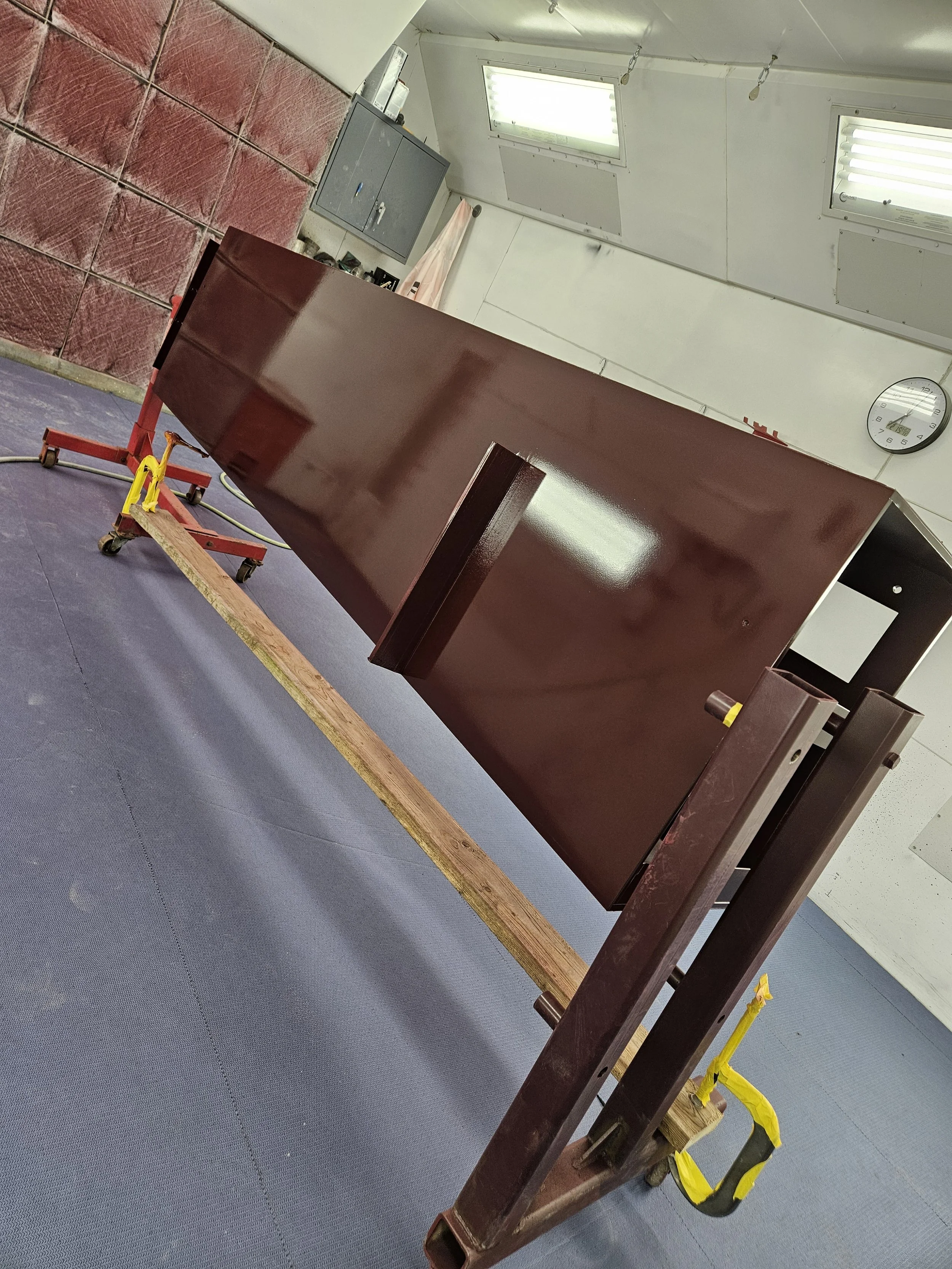 Large wooden cabinet or piece of furniture being moved or assembled with a red dolly and yellow straps in a workshop or storage room.