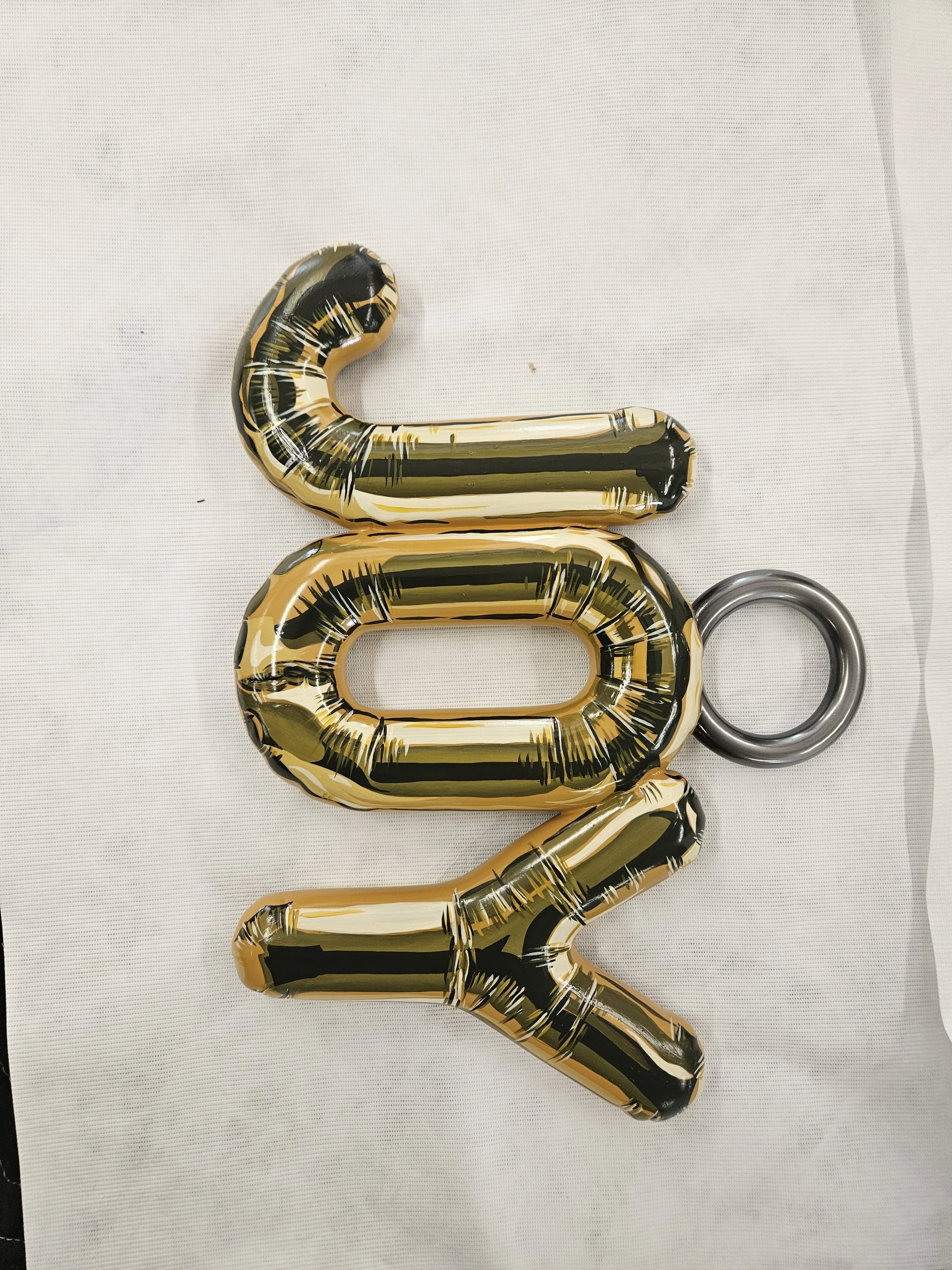Gold and black letter balloons spelling out 'LOVE' with a metallic ring on the right side, lying on white fabric background.
