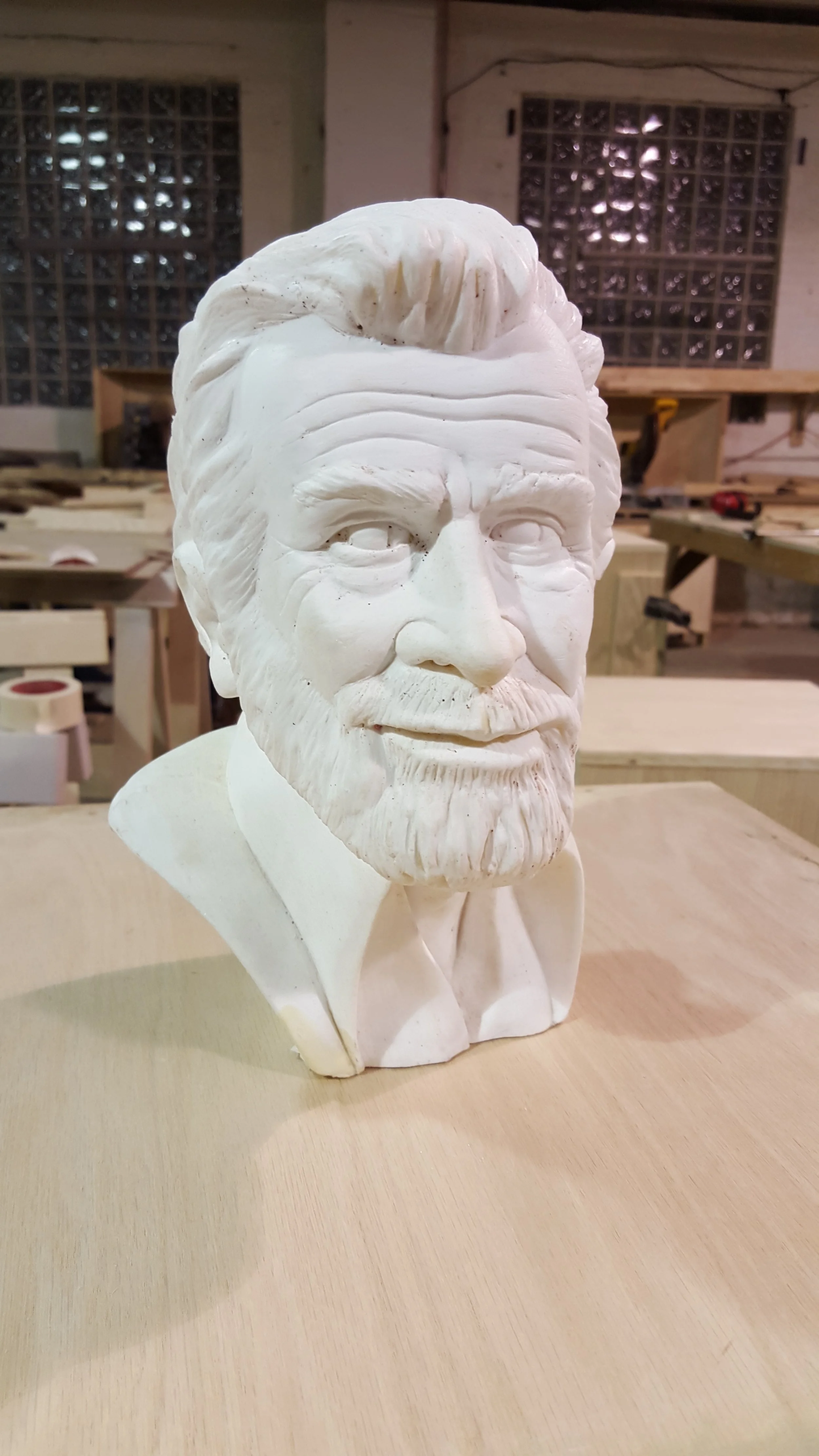 White plaster bust of a bearded man with combed-back hair in a woodworking shop.