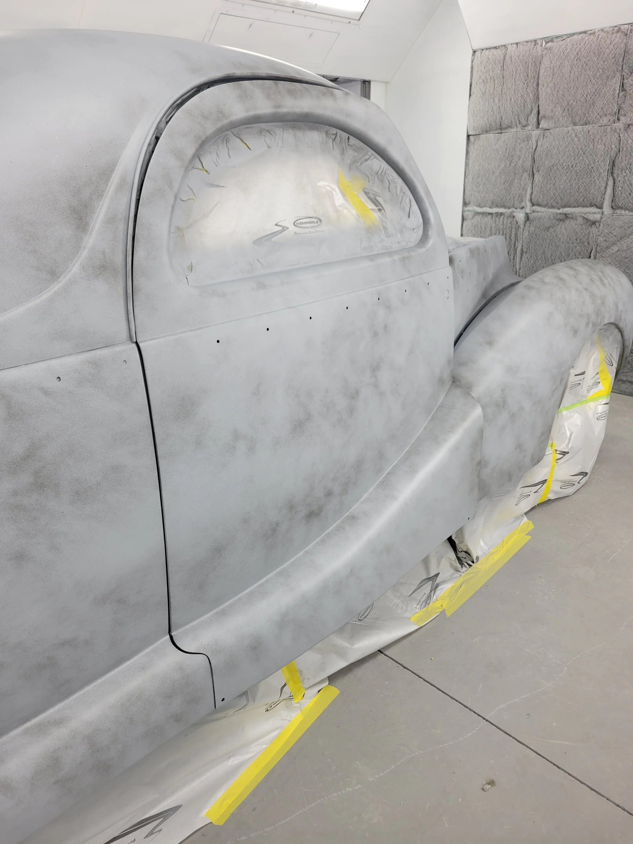 A car in the process of being painted, covered with primer, and masked with paper and tape for painting.