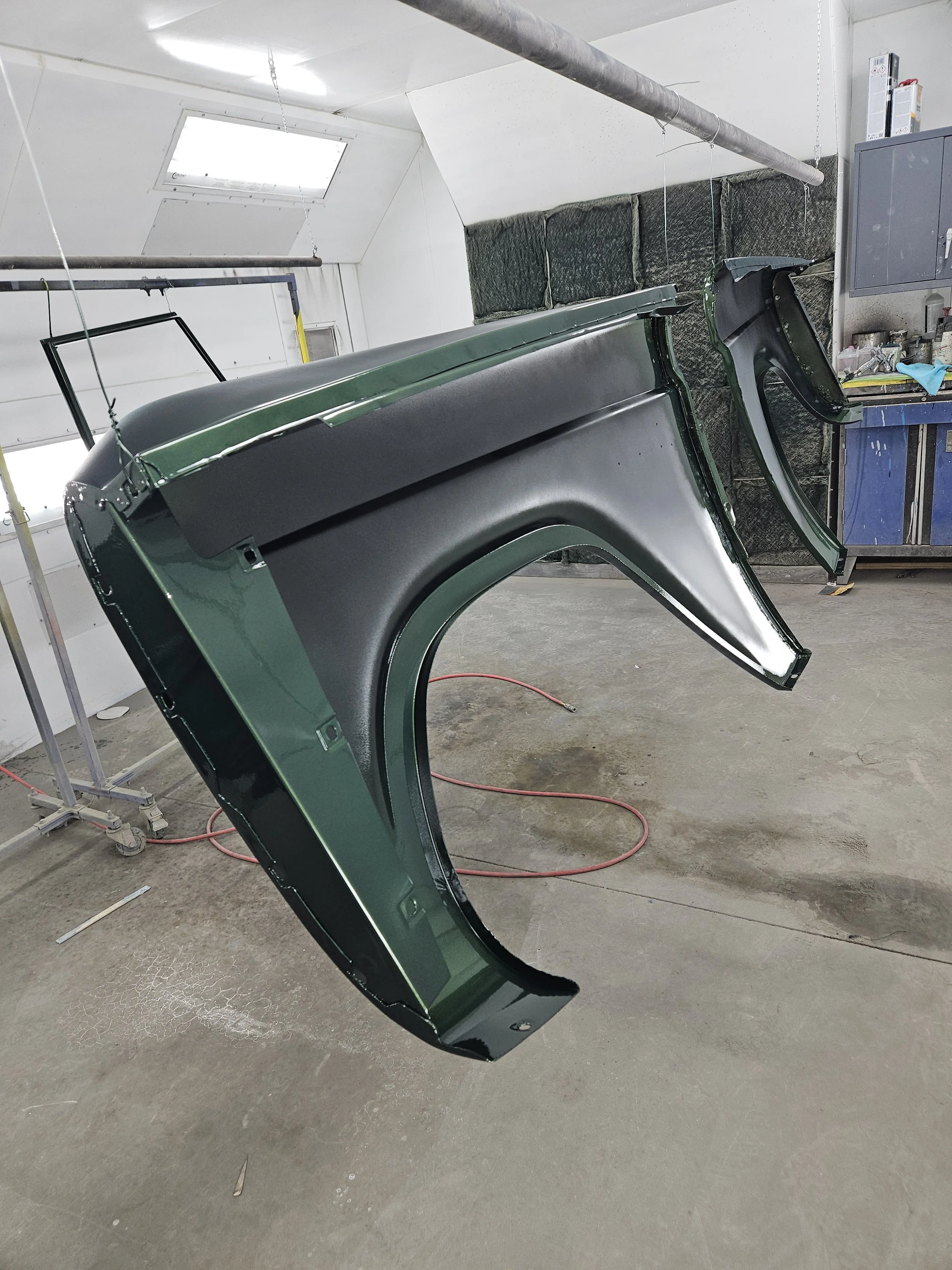 Car fenders painted in black and green hanging in a workshop.