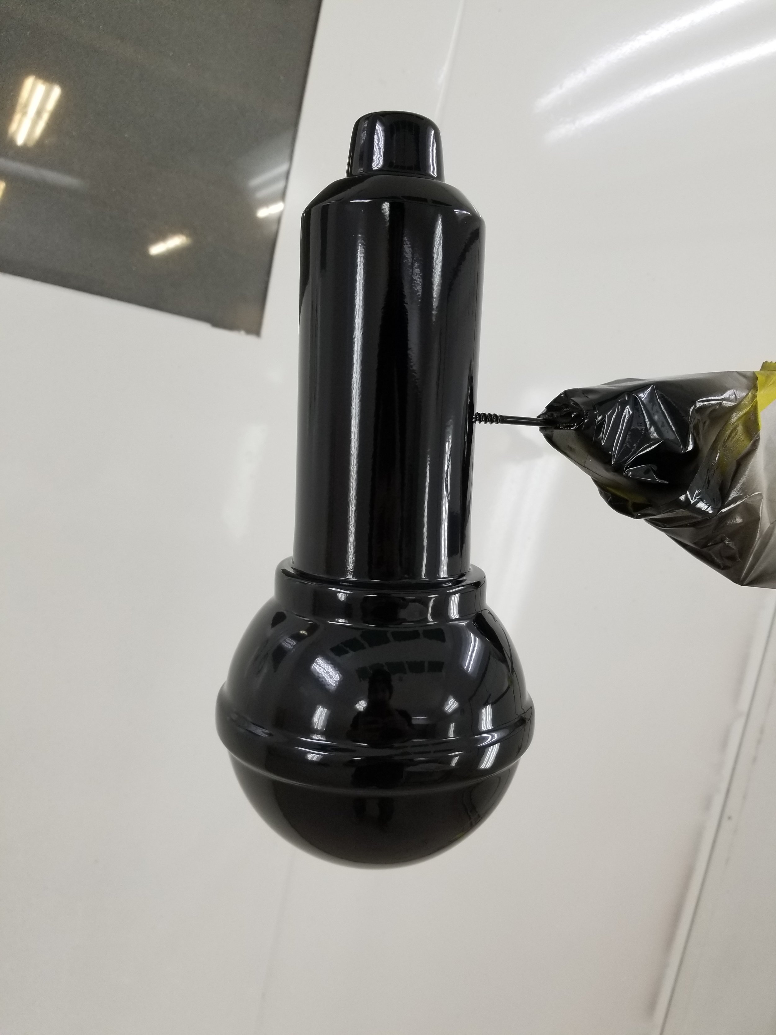 A black, glossy, capsule-shaped object hanging upside down from a person's gloved hand in an indoor setting.