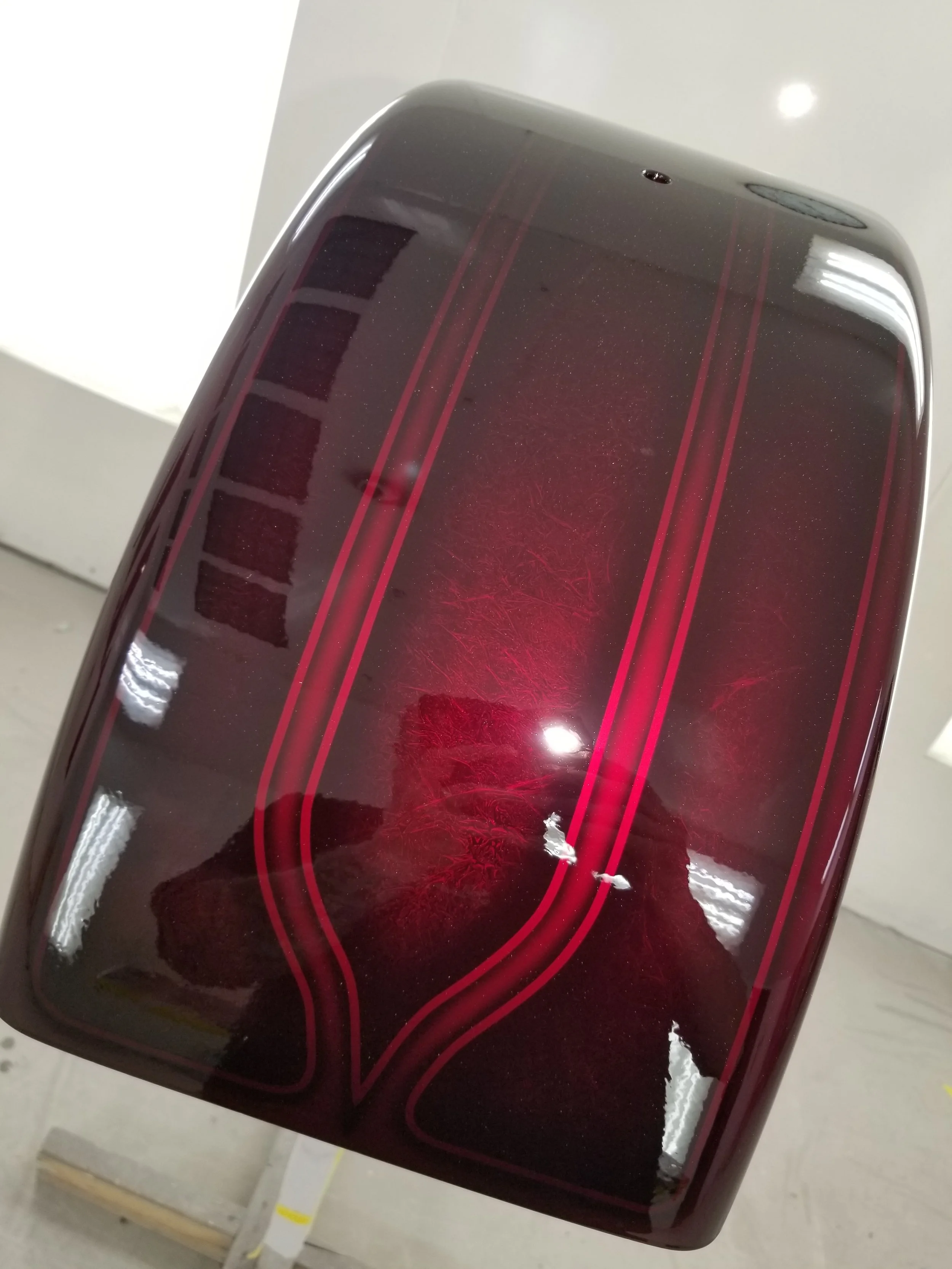 Close-up of a shiny, dark red motorcycle part with red pinstripes and a subtle pattern visible on the surface.
