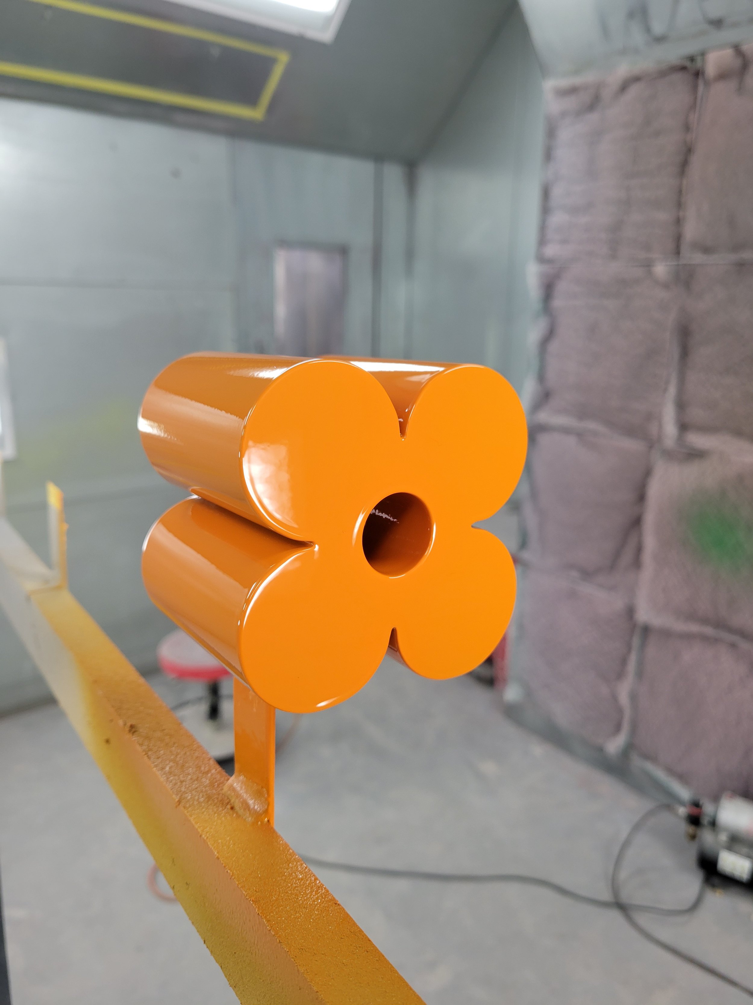 Orange flower-shaped object made of glossy metal, mounted on a yellow railing.