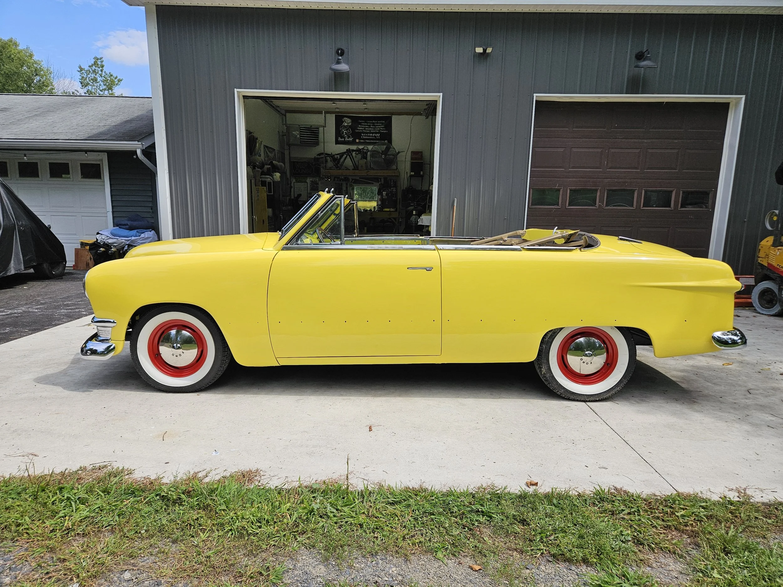 Yellow vintage convertible car with red and white wheels parked outside a garage.