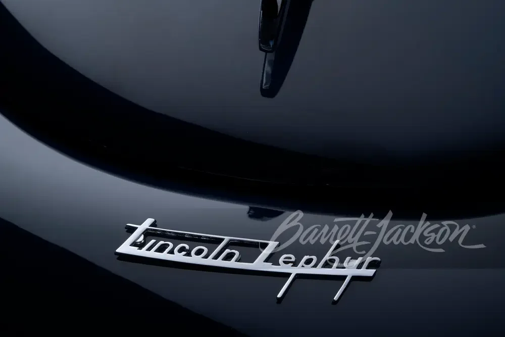 Close-up of a classic Lincoln Zephyr hood ornament on a black car with a Barrett-Jackson logo in the background.