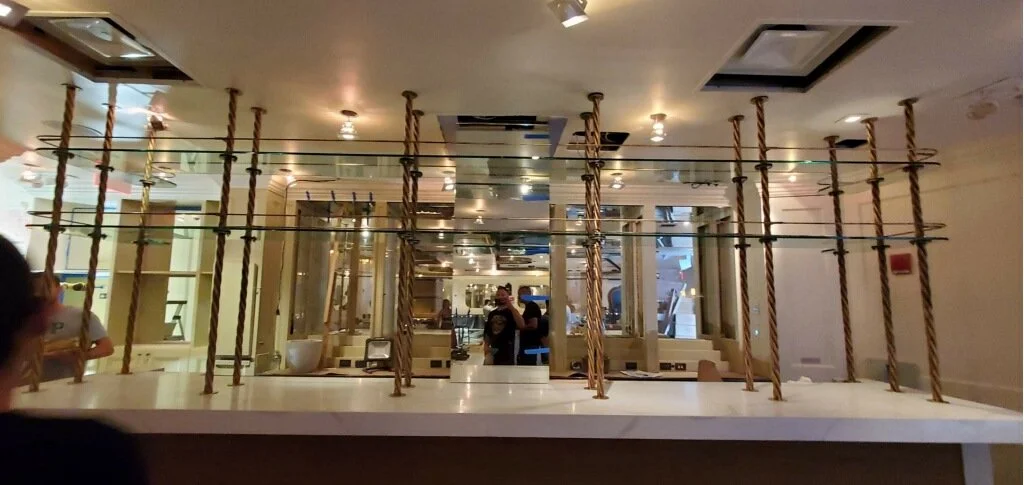 Empty restaurant bar with rope and wood shelf dividers, reflective ceiling, and some people in the background.