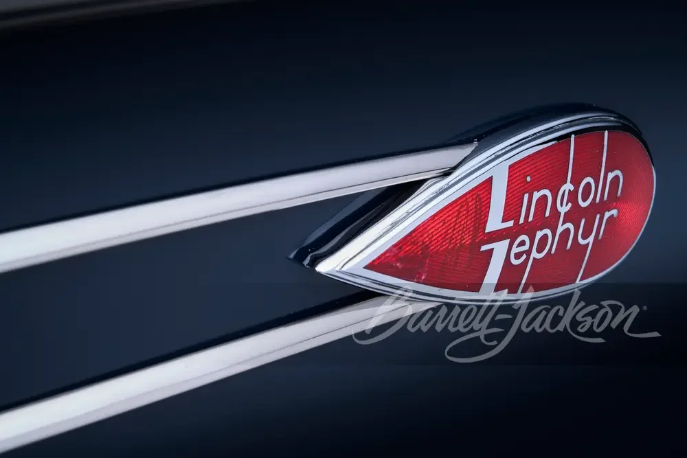 Close-up of a vintage car's tail fin with a decorative red and white emblem reading "Lindon Zephyr."