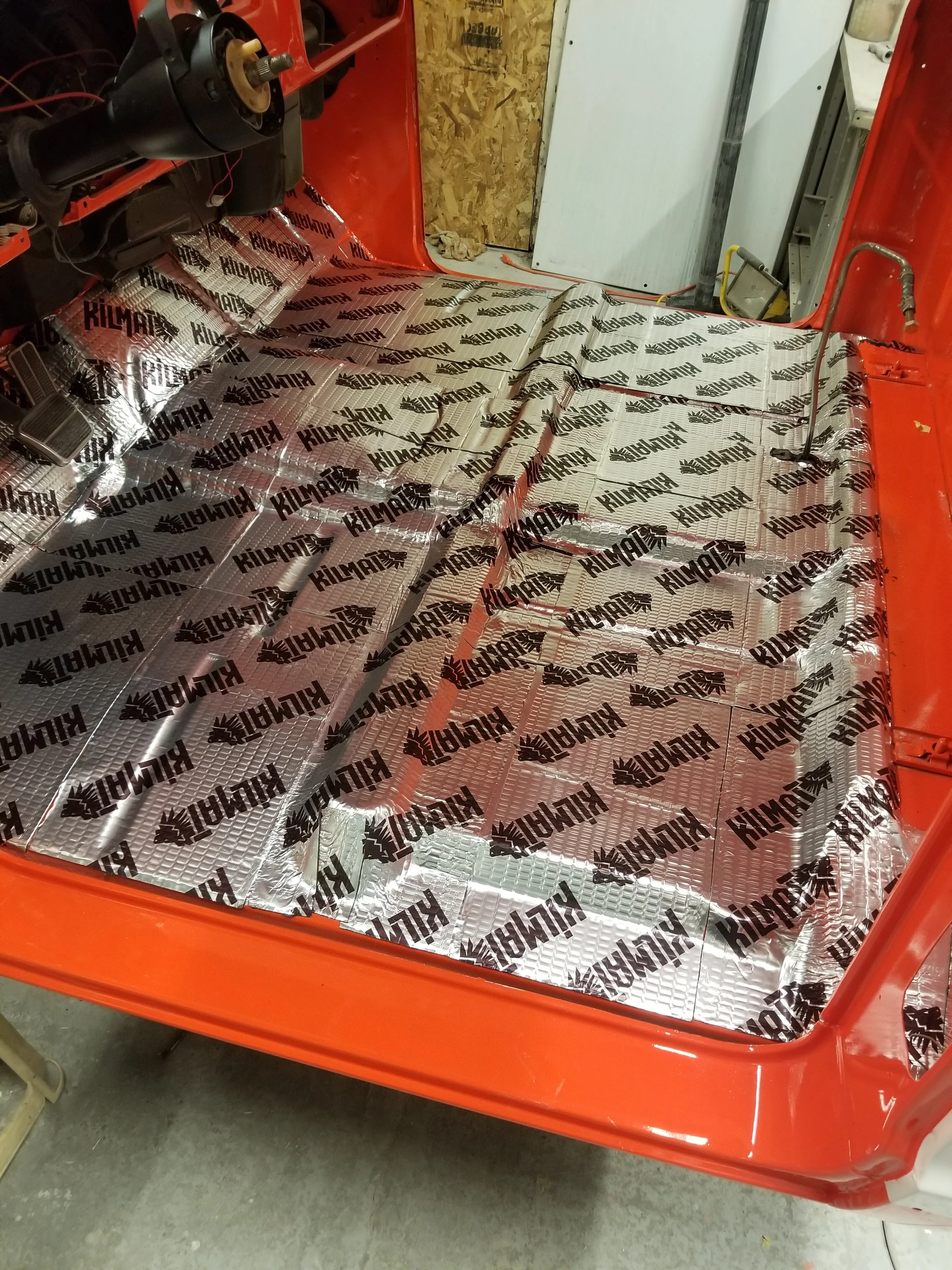 The interior of a vehicle being soundproofed with Kilmat sound deadening mats partially installed over the floor.