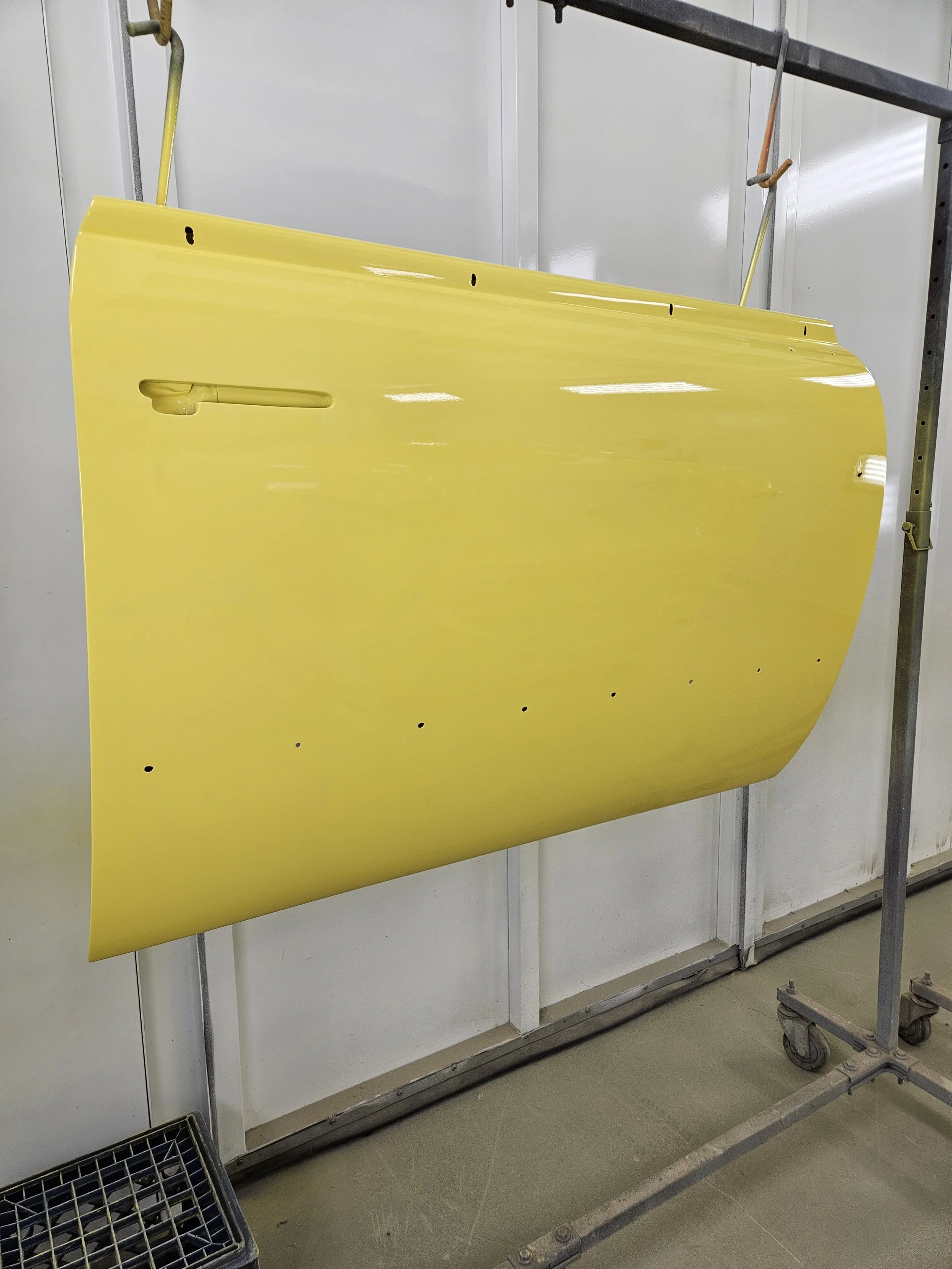 A yellow car door hanging on a stand in a workshop or manufacturing area.
