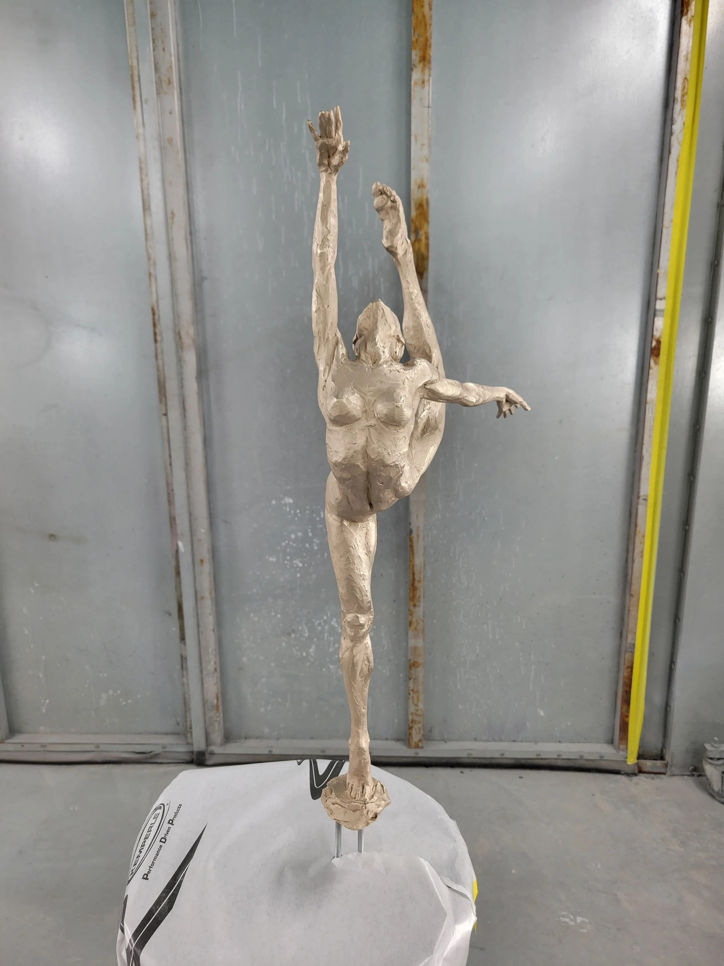 A detailed sculpture of a ballet dancer in a dynamic pose, standing on one leg with arms raised and head tilted back, painted in a metallic gold color.