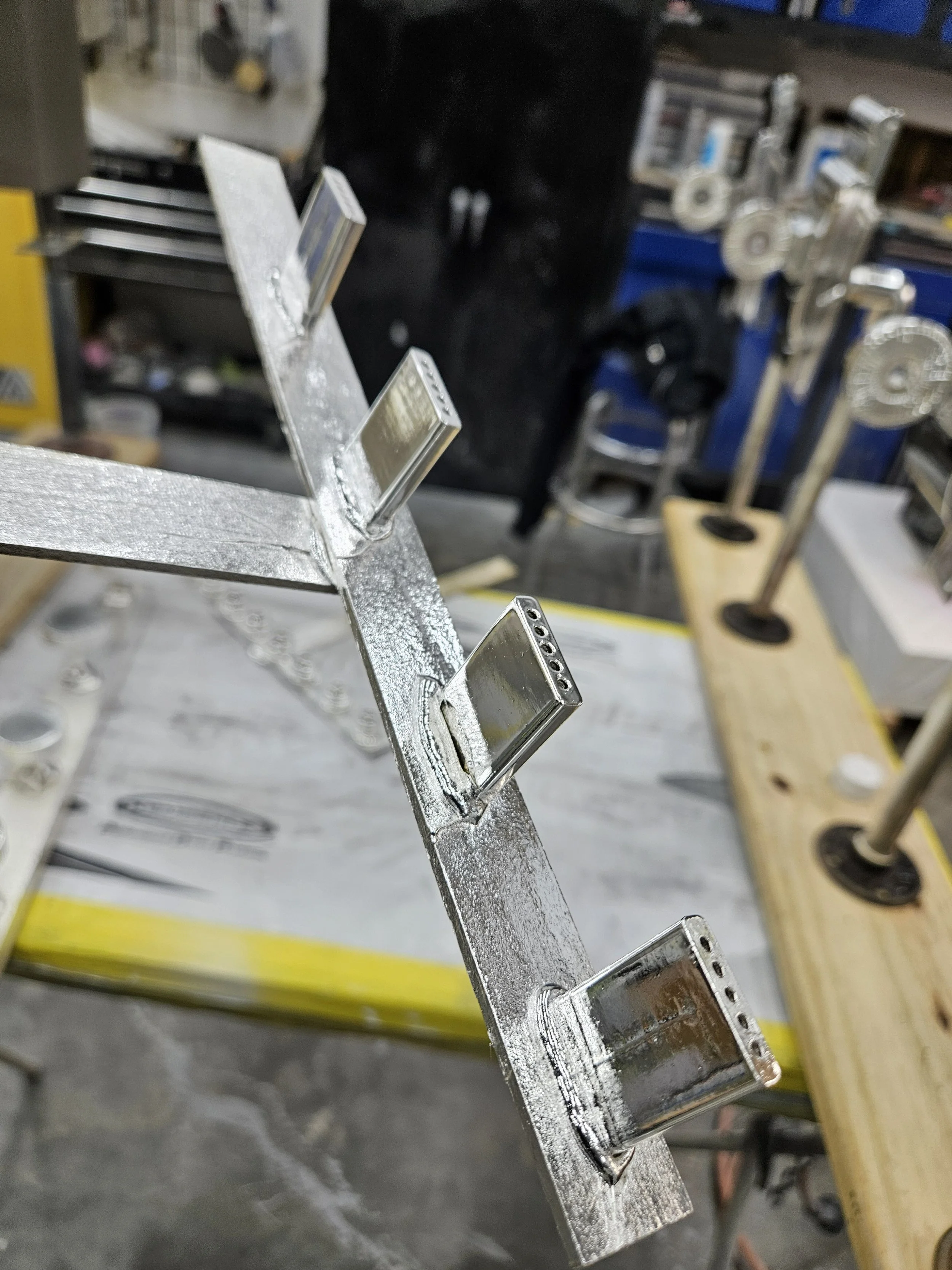 Metal structure with rectangular tubes welded onto a flat metal strip in a workshop.