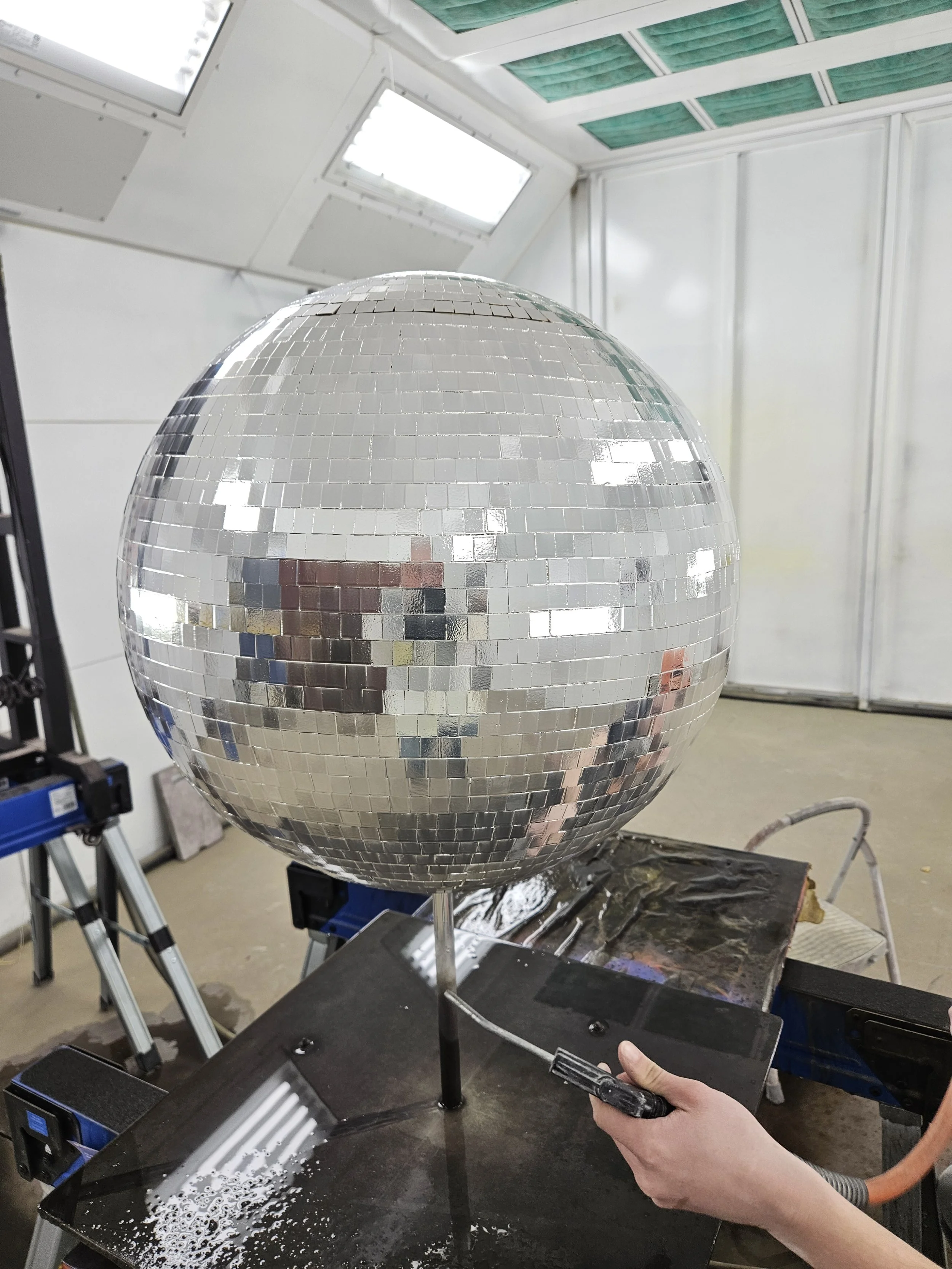 Disco ball being cleaned or polished in a workshop with tools and equipment around.