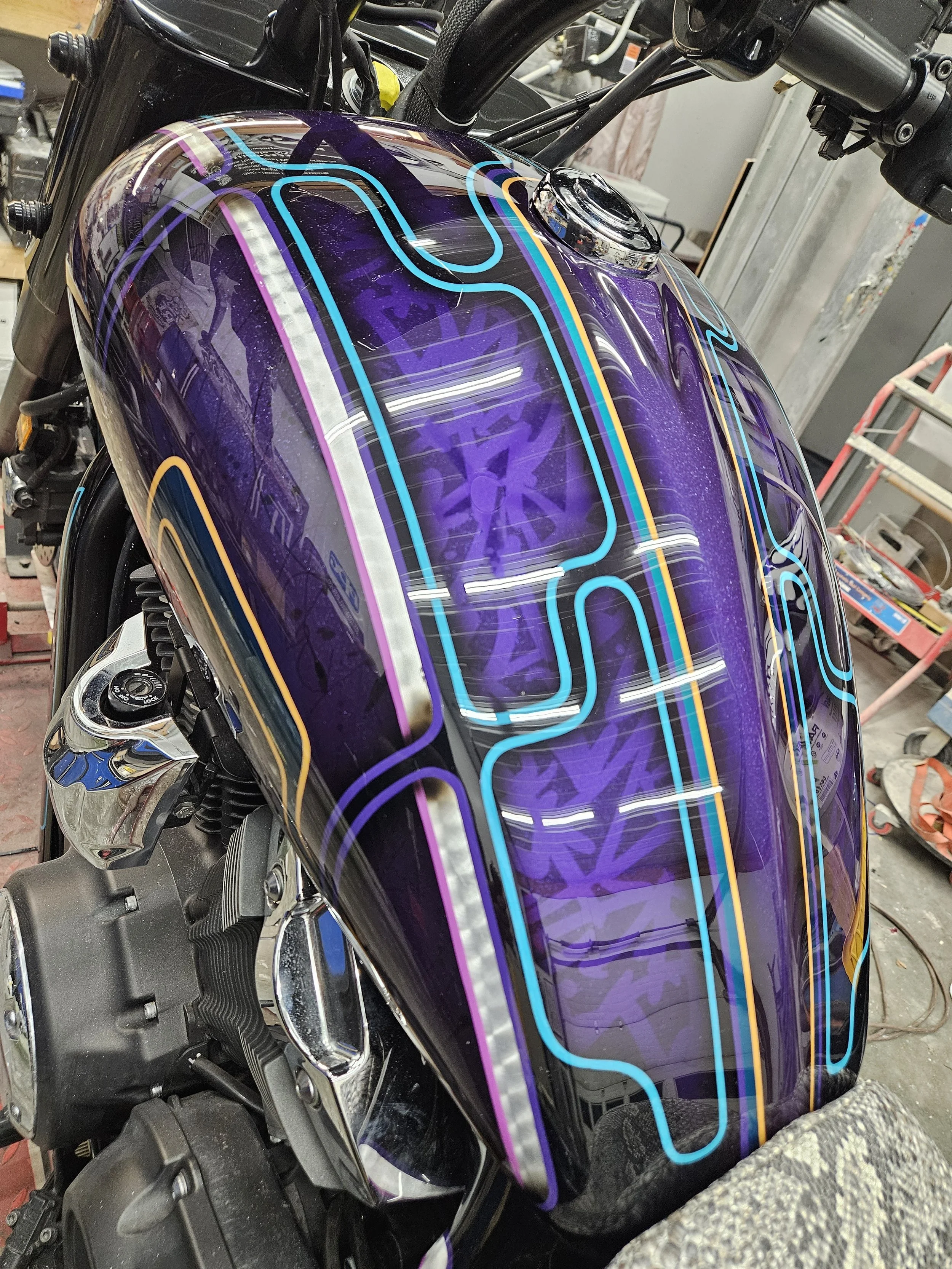 Close-up of a motorcycle fuel tank with a neon stripe design on a purple background.