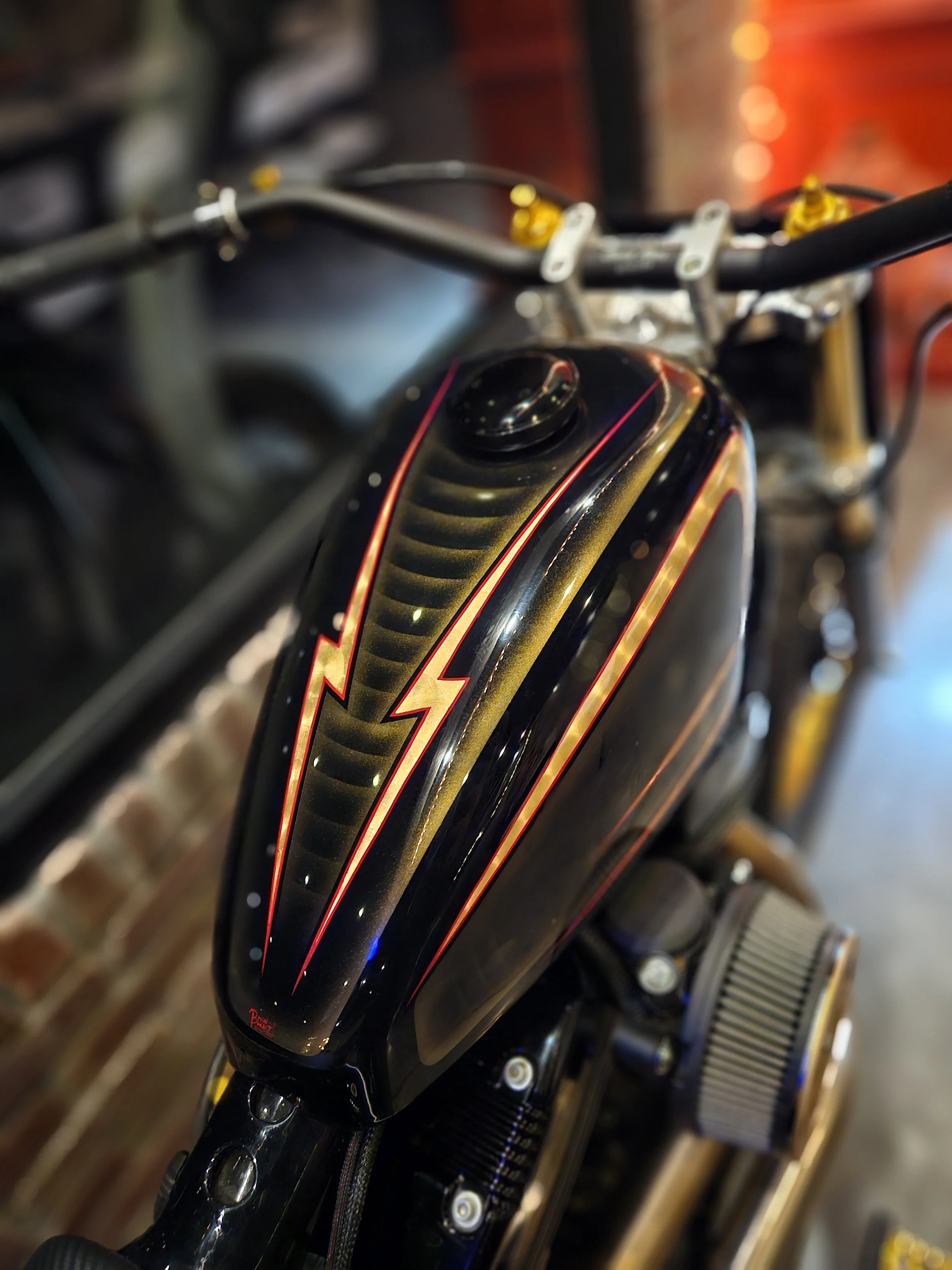 Close-up of a black motorcycle gas tank with red and gold lightning bolt design.