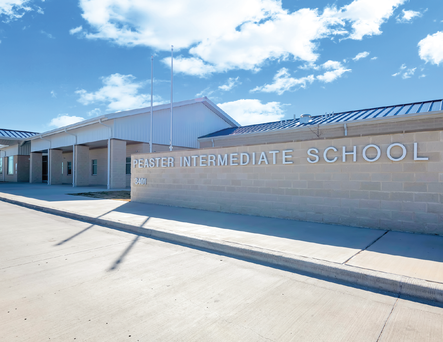 Exterior of Peaster Intermediate School building with blue sky and clouds, showing the school's name on the front wall