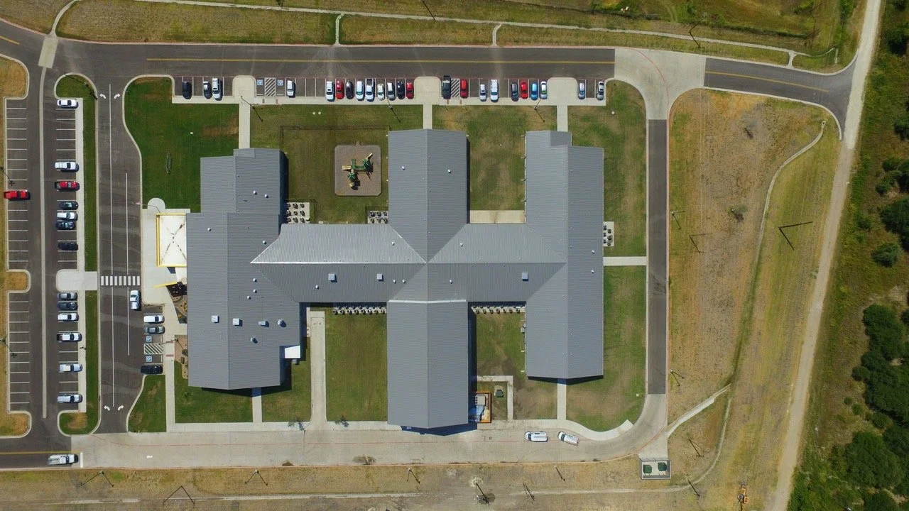 Aerial view of a school building with a surrounding parking lot and green fields.