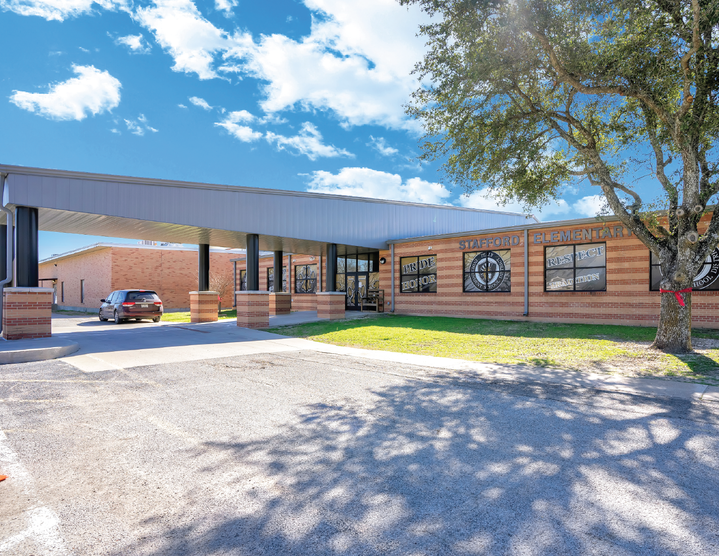 Exterior view of Stafford Elementary School with a brick facade, tree, parking lot, and sunny sky.