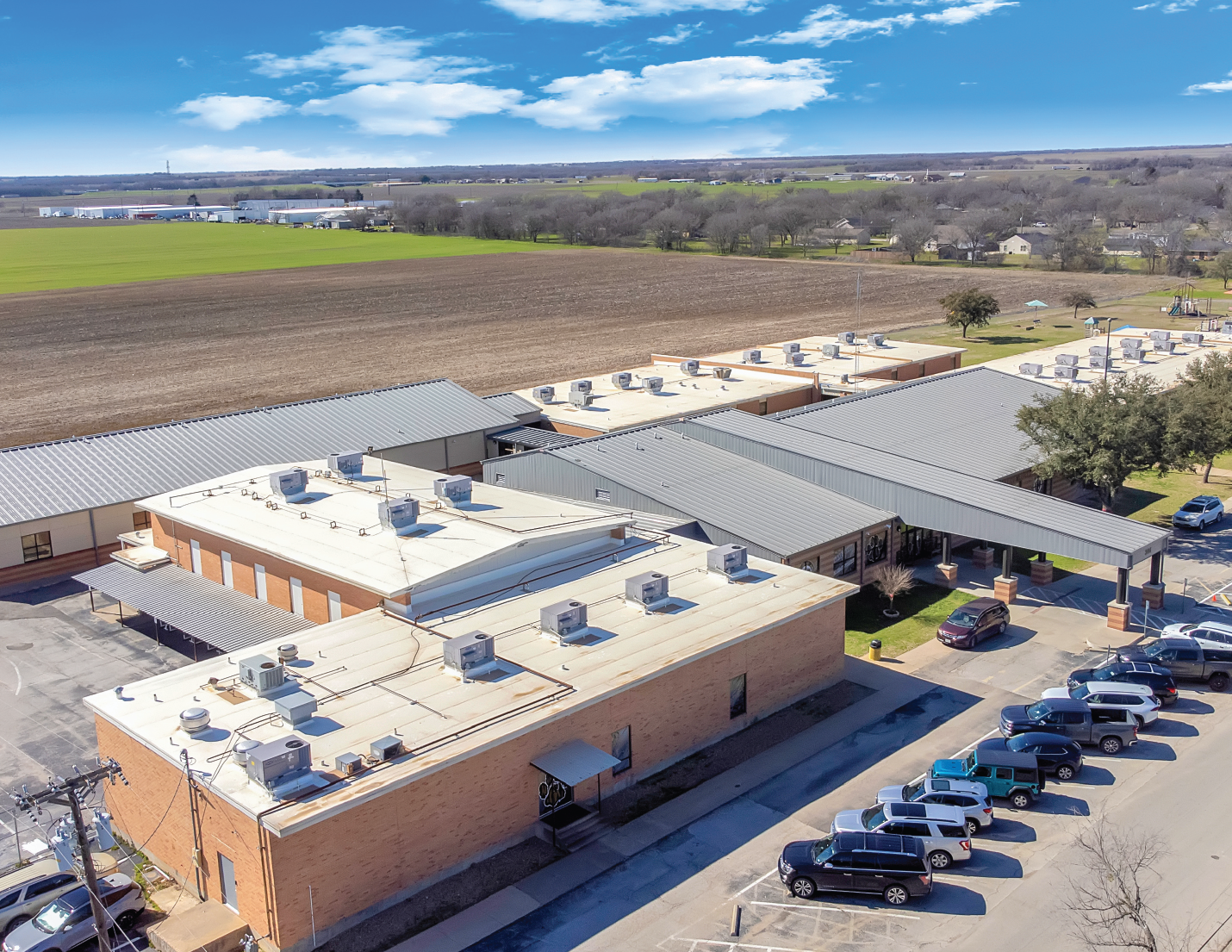 An aerial view of a school building with parking lot and surrounding fields under a partly cloudy sky.