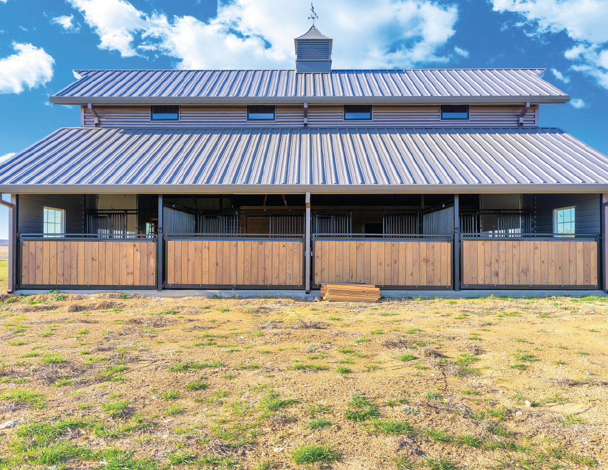Front view of a modern barn-style building with a metal roof, black and wood siding, and a large porch area.