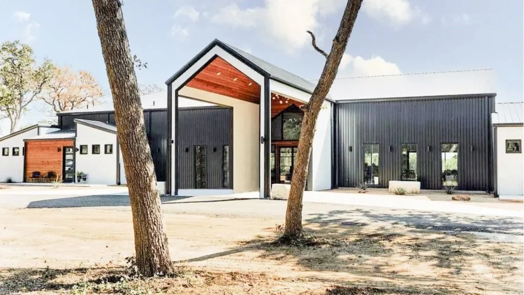 Modern building with a mix of white and dark gray exterior walls, large windows, and two trees in the foreground.
