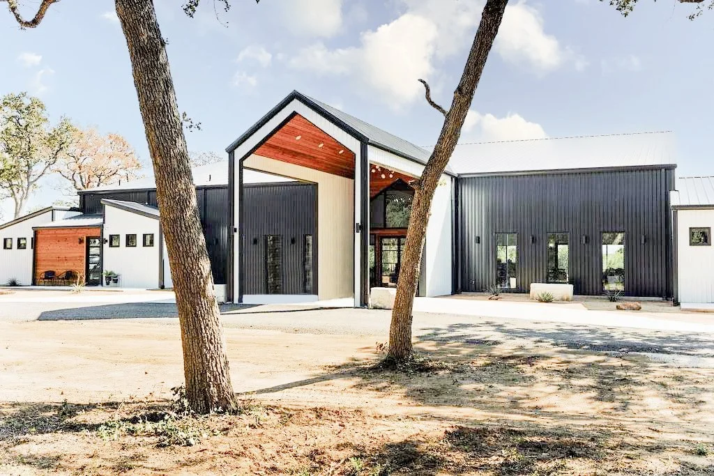 Modern barn-style building with black, white, and wood exterior, set among trees on a clear day.