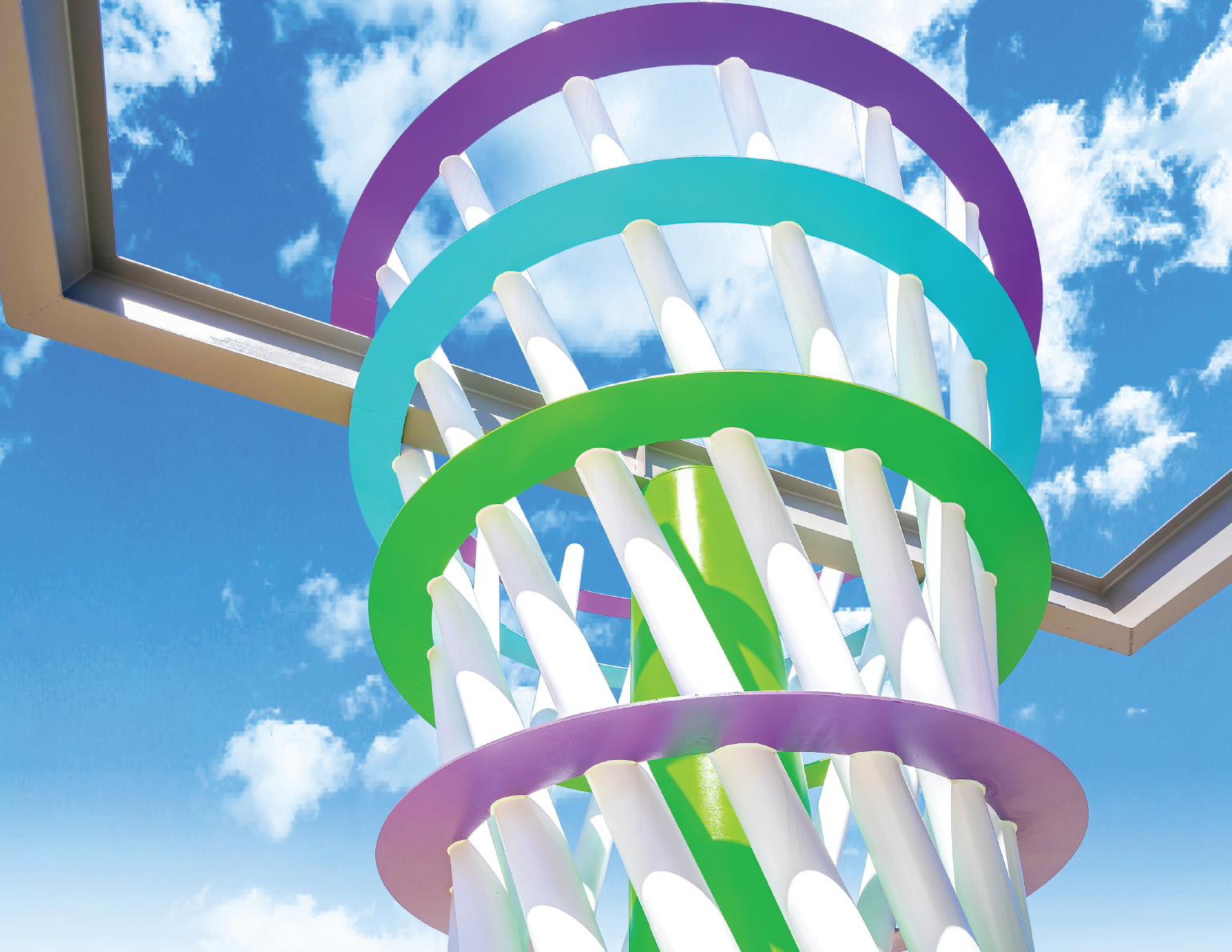Colorful modern outdoor basketball hoop with green, blue, and purple rings, set against a bright blue sky with white clouds.