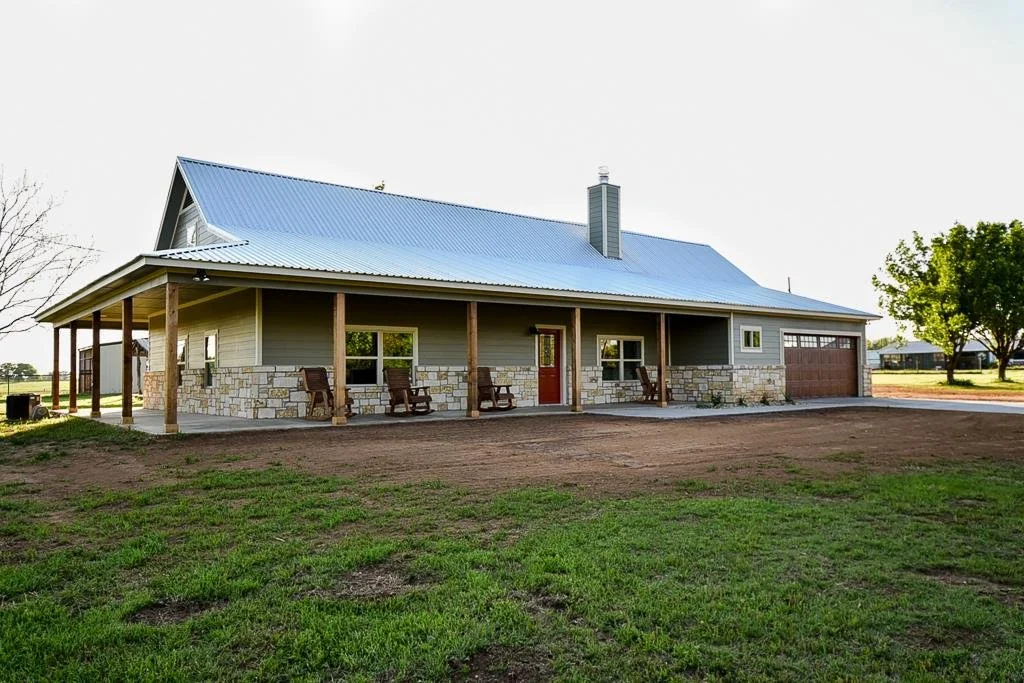 A large house with a blue metal roof, stone accents, and a covered porch with wooden rocking chairs.