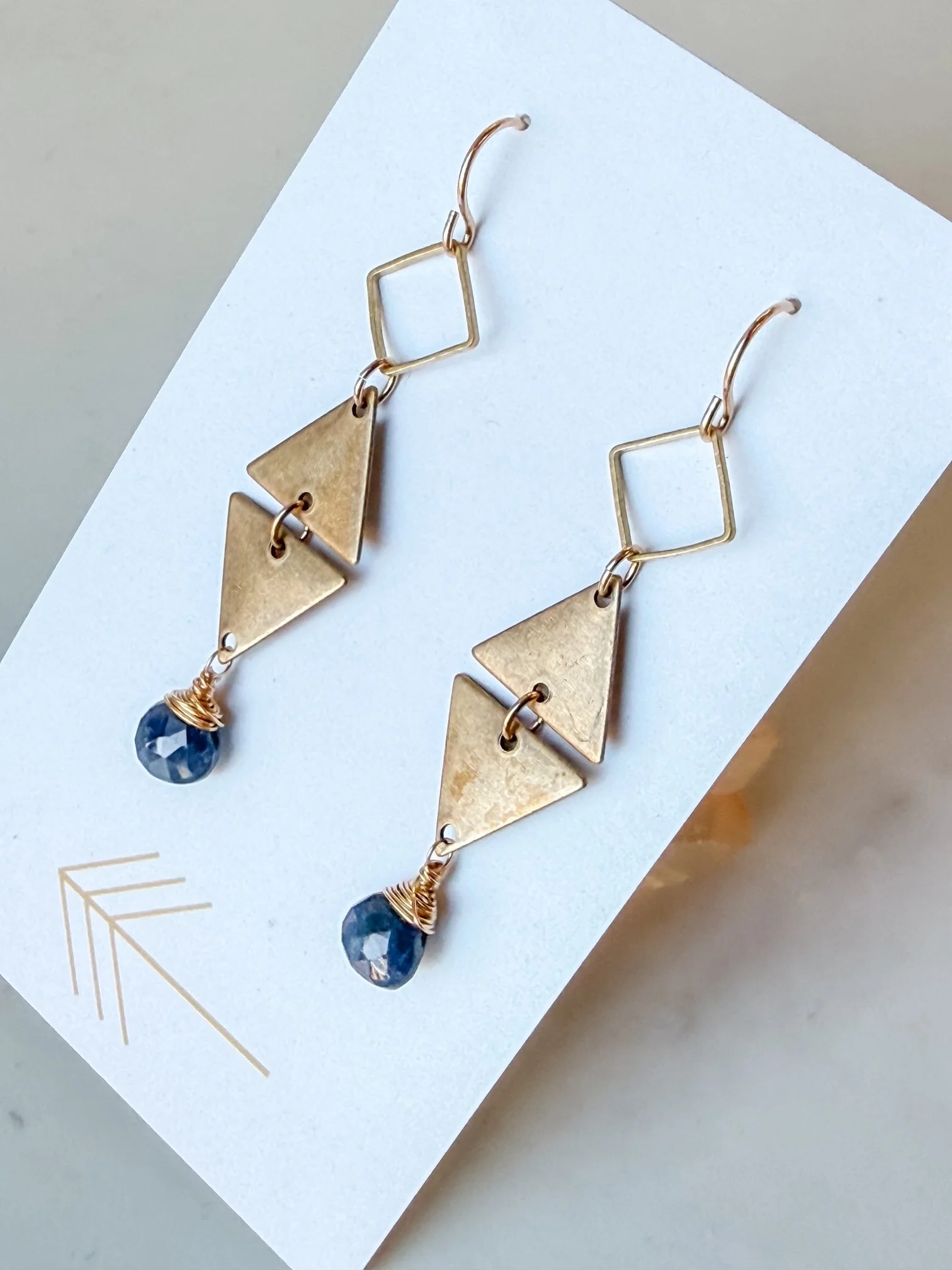 Gold geometric dangle earrings with black gemstone beads on white jewelry card.