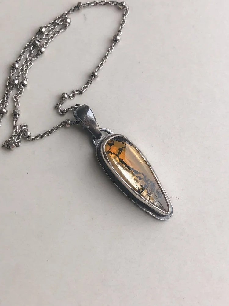 You can see orange iron oxides fill most of this teardrop shaped Quartz stone. The branch-like dendrites run throughout. The chain features tiny faceted beads. The stone is rests in a hand-dipped, two-toned setting.