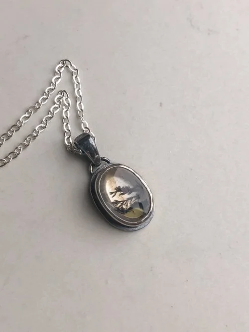 You can see faint yellow iron oxides in this oval shaped Quartz stone. The branch-like dendrites run throughout. The stone is rests in a hand-dipped, two-toned setting.