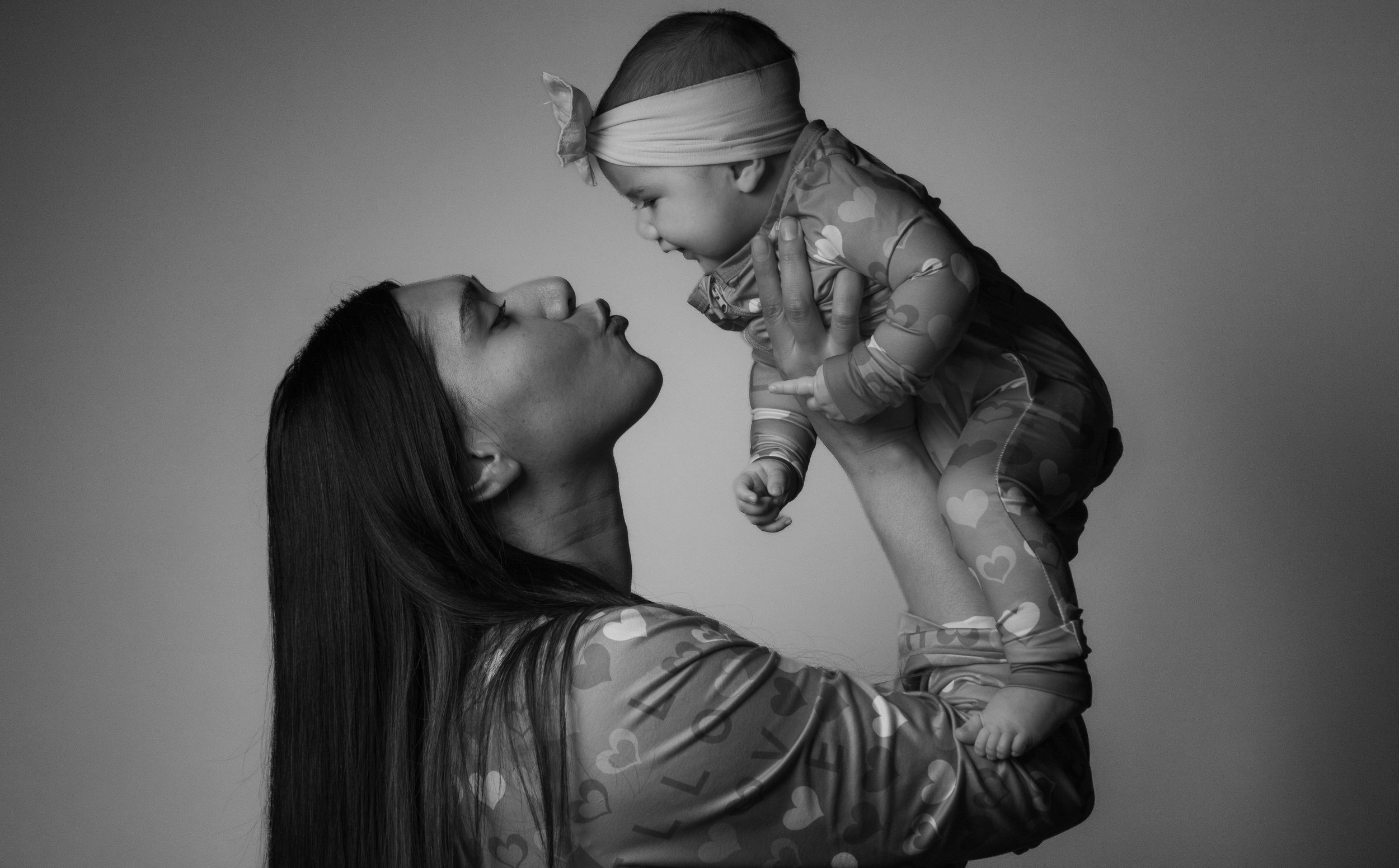 A woman holding a baby up in the air, both facing each other, in an intimate moment. The image is in black and white.