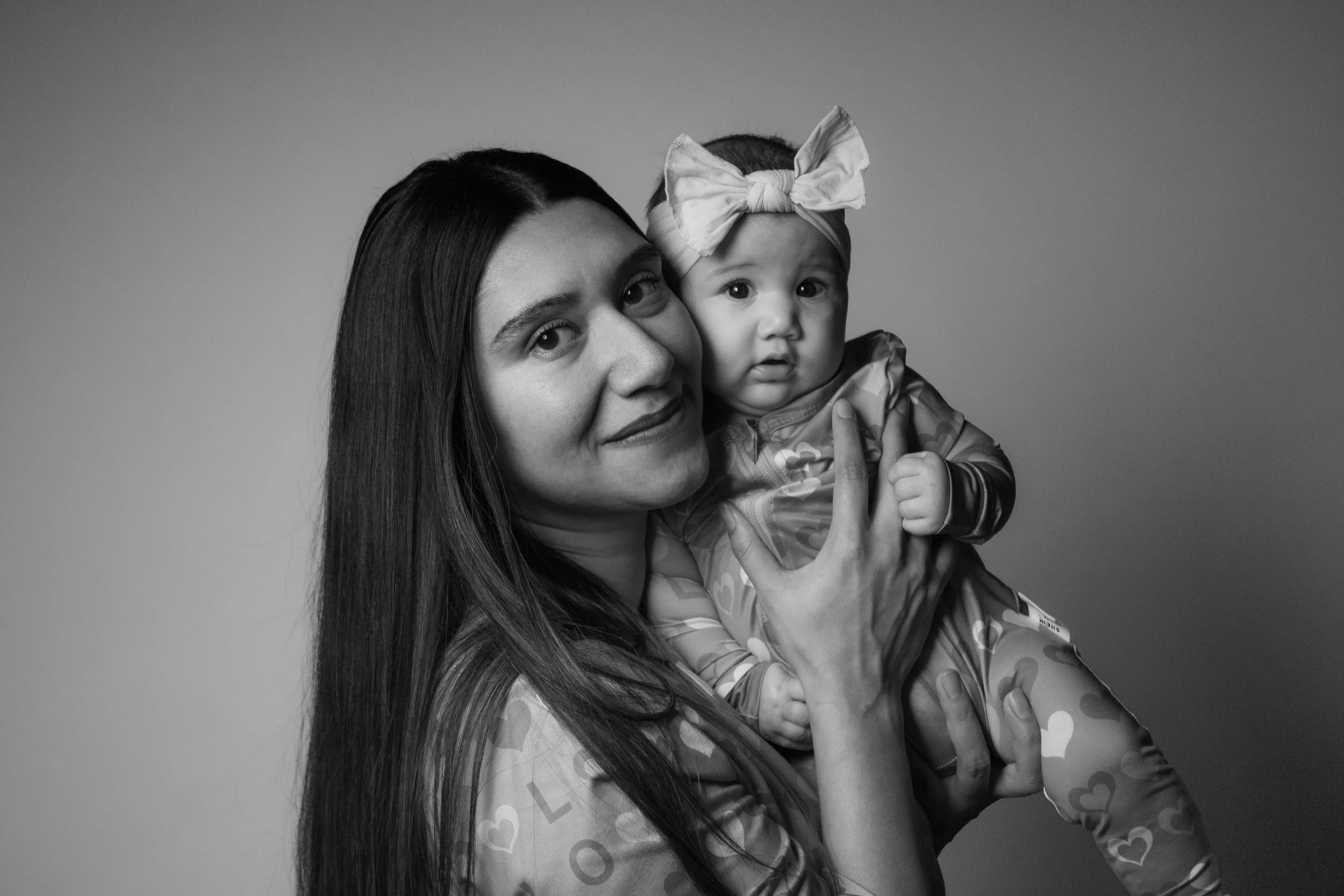 A woman with long dark hair holding a young girl with a bow headband, both looking at the camera, black and white photo.