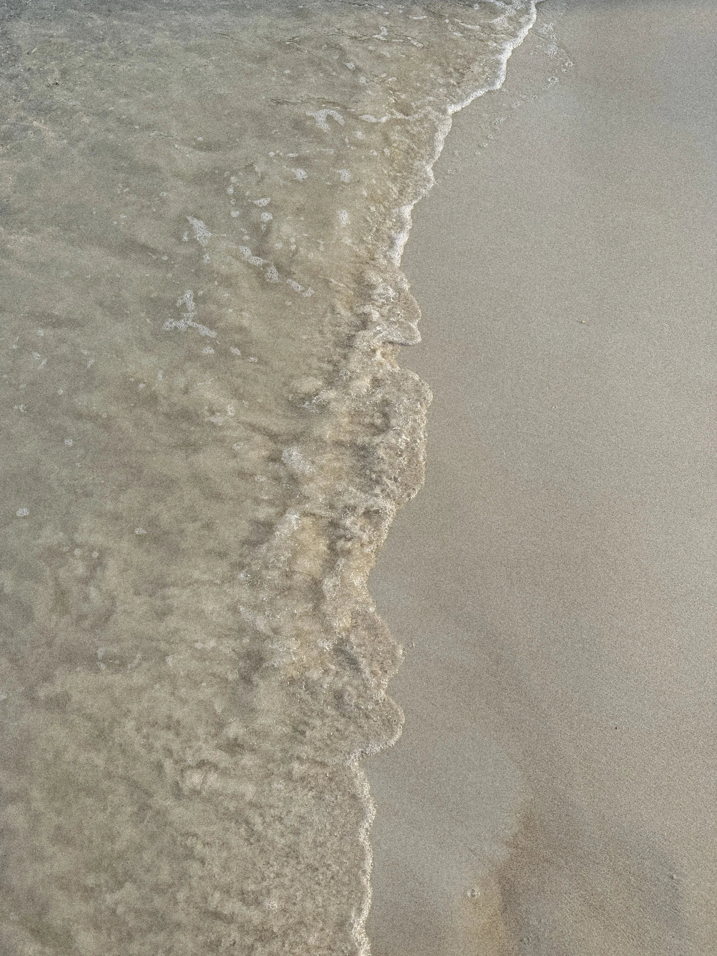 Close-up of waves gently washing onto a sandy beach.
