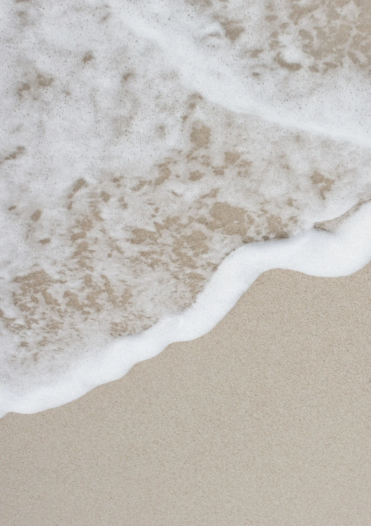 Close-up of a wave gently washing onto a sandy beach.